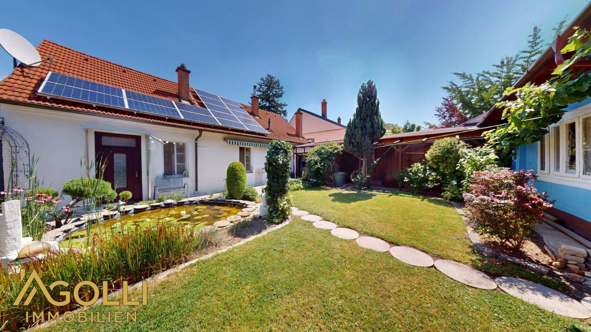 Sonniger Garten mit Zierteich, grünen Pflanzen und Solaranlage auf dem Dach.