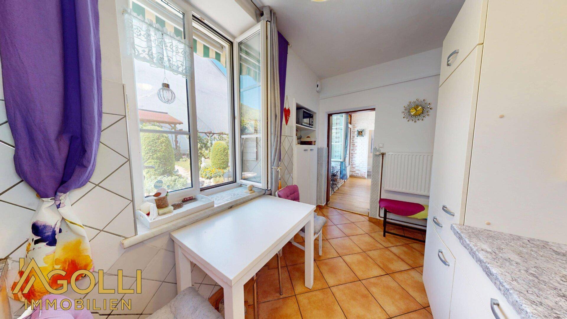 Helle Küche mit Esstisch am Fenster und Blick auf den grünen Gartenbereich.
