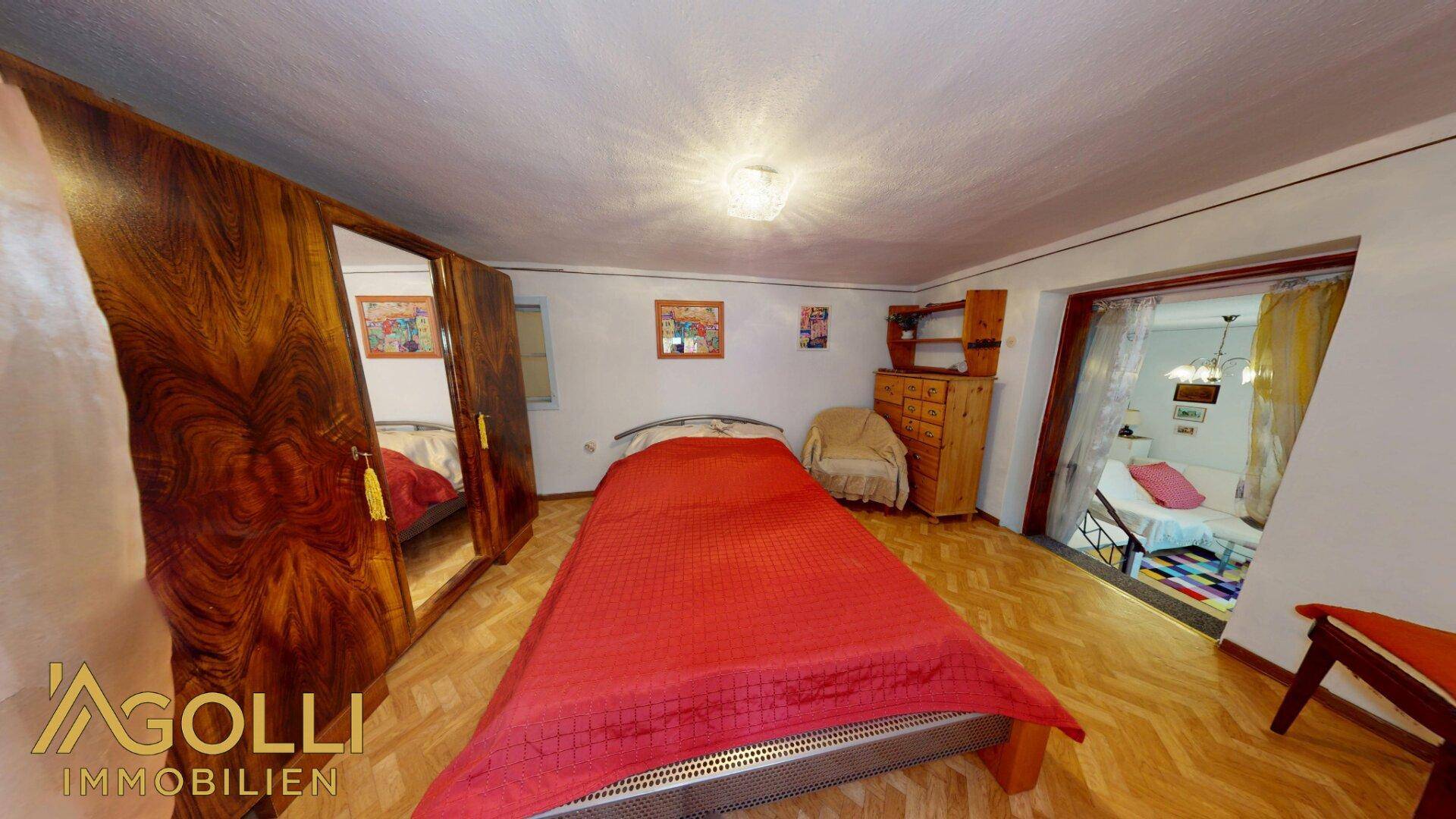 Schlafzimmer mit Holzboden, großem Schrank und offenem Zugang zu einem weiteren Raum.