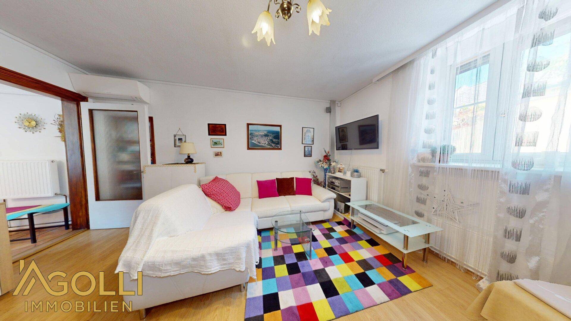 Gemütliches Wohnzimmer mit Sofa, farbenfrohem Teppich und viel Tageslicht durch das Fenster.