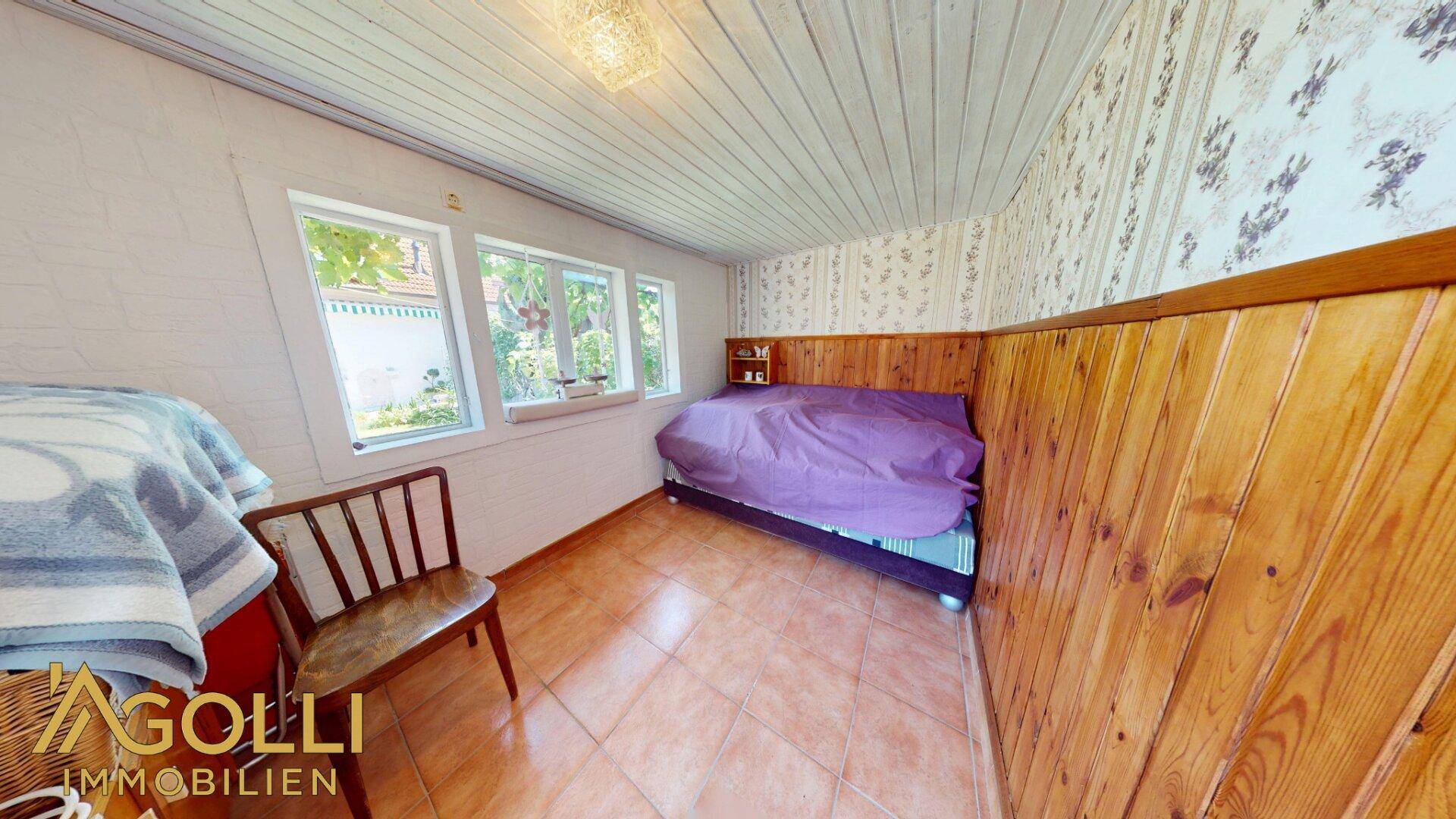 Kleines Zimmer mit Holzvertäfelung, Fliesenboden und Blick in den Garten.