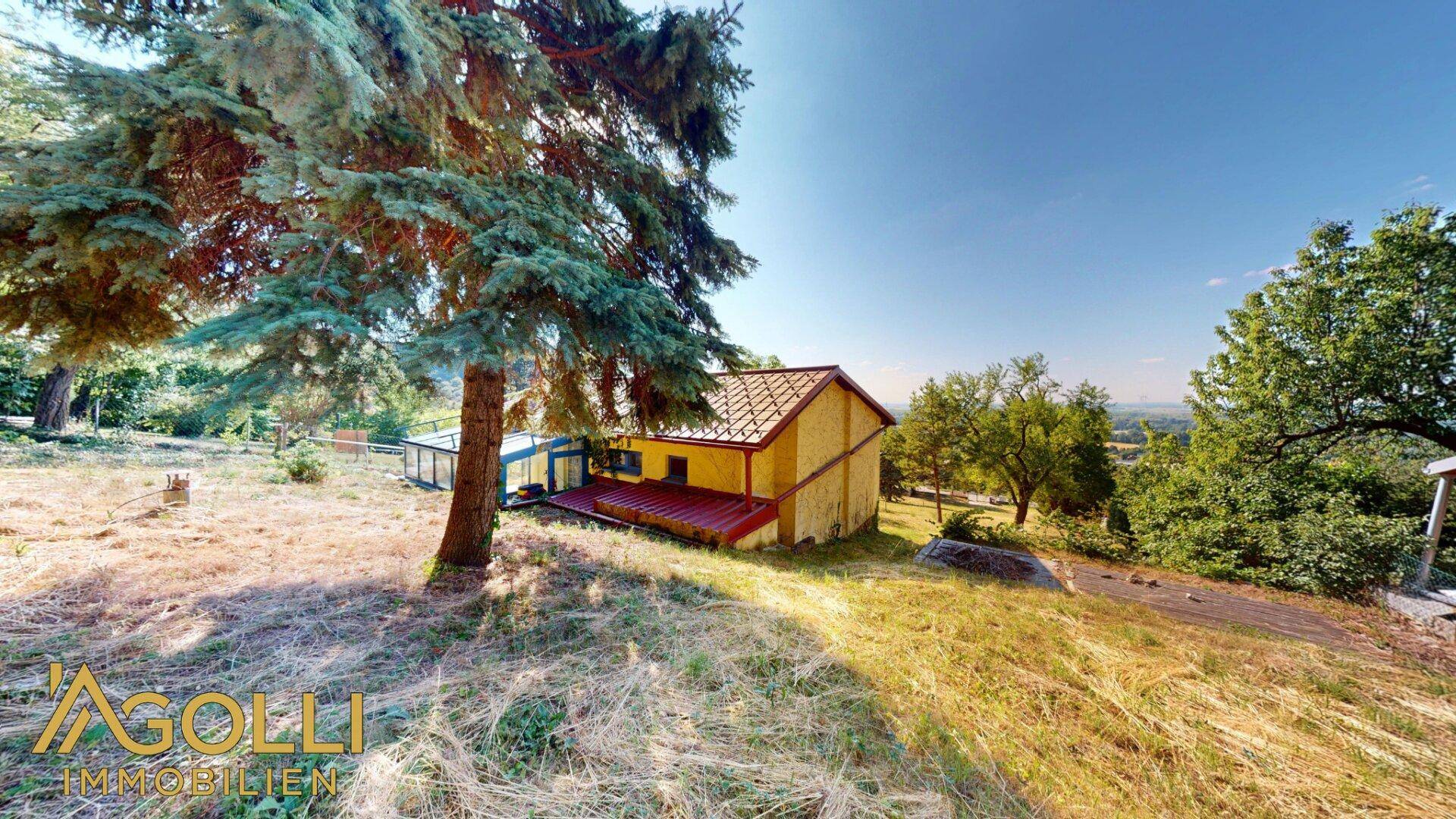 Freistehendes Haus mit rotem Dach und angrenzendem Wintergarten in ländlicher Umgebung.