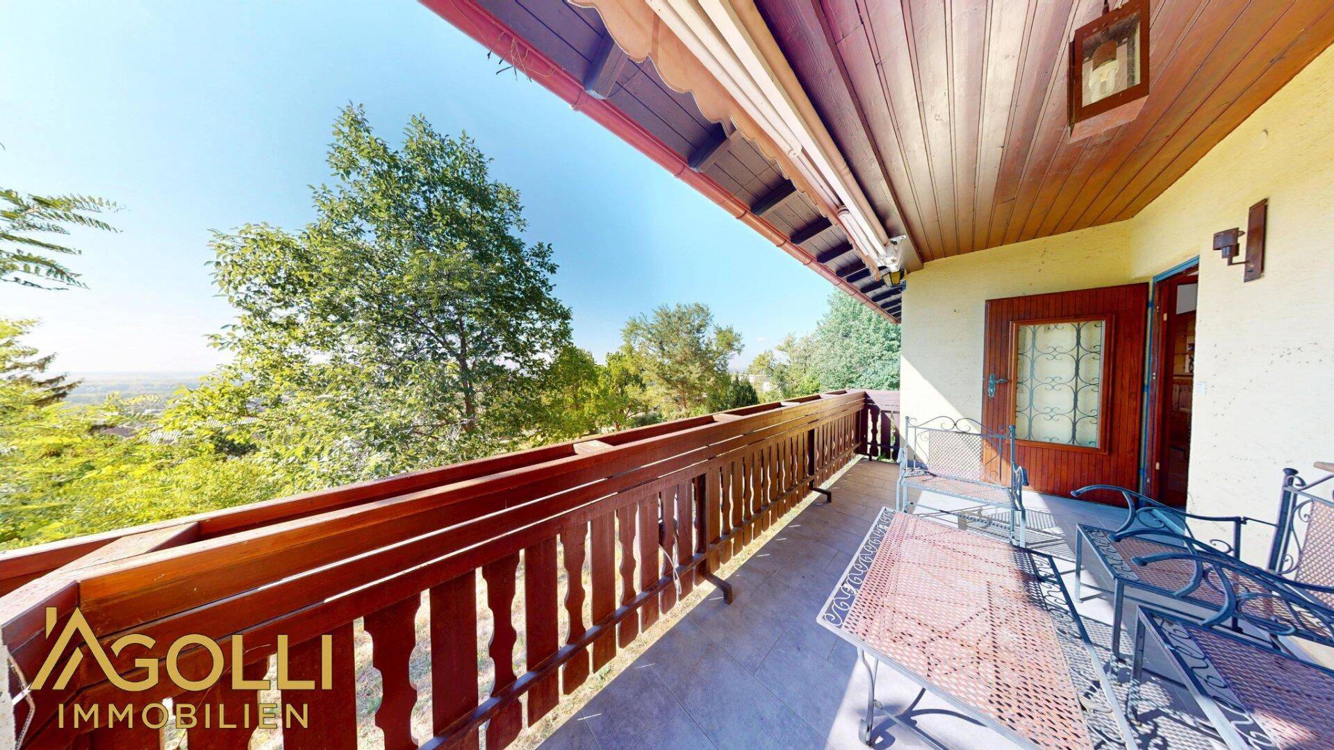 Geräumiger Balkon mit Holzgeländer, Sitzgelegenheiten und weitem Ausblick.
