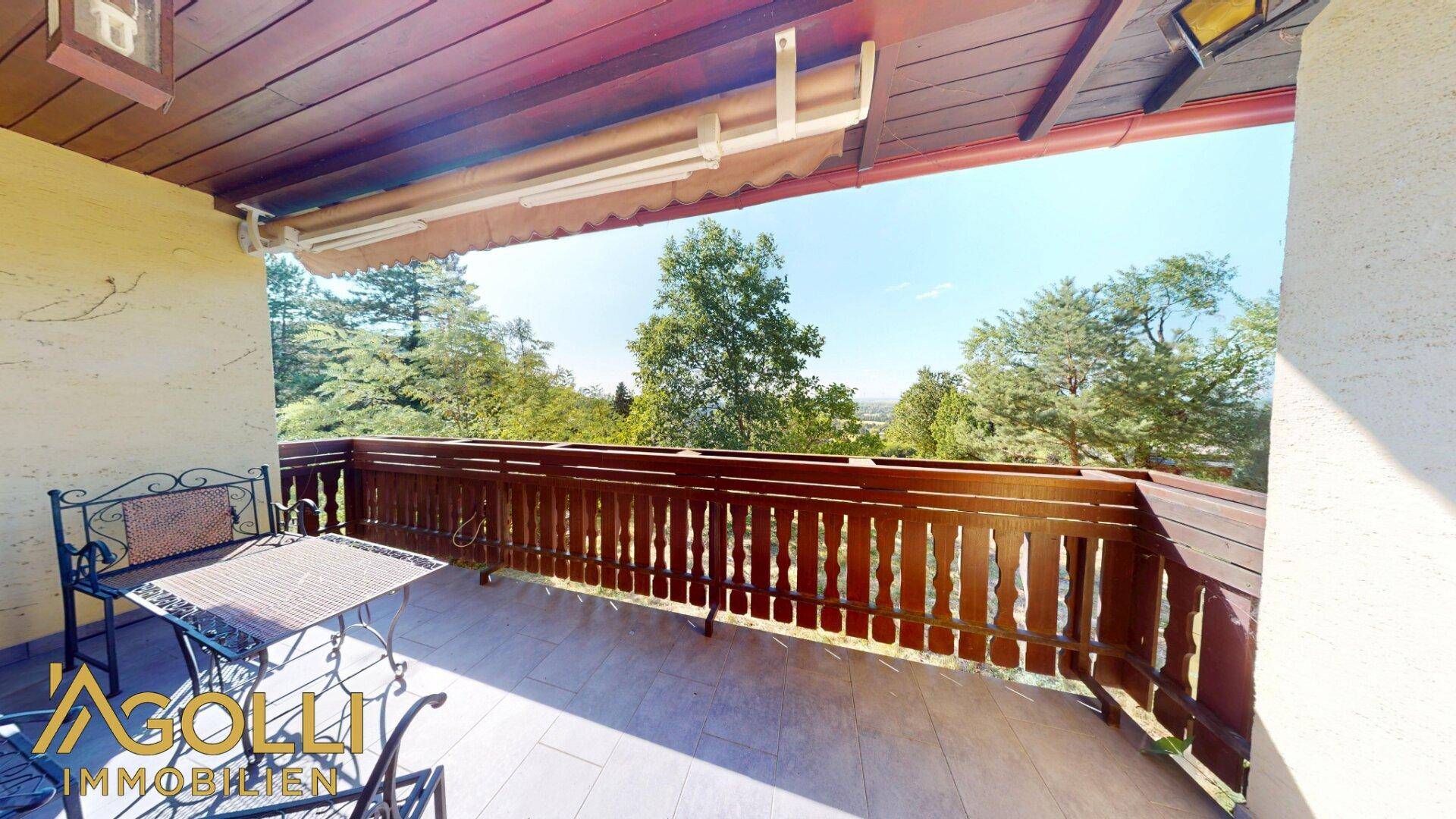 Sonniger Balkon mit traditionellem Holzgeländer und Blick in die Natur.