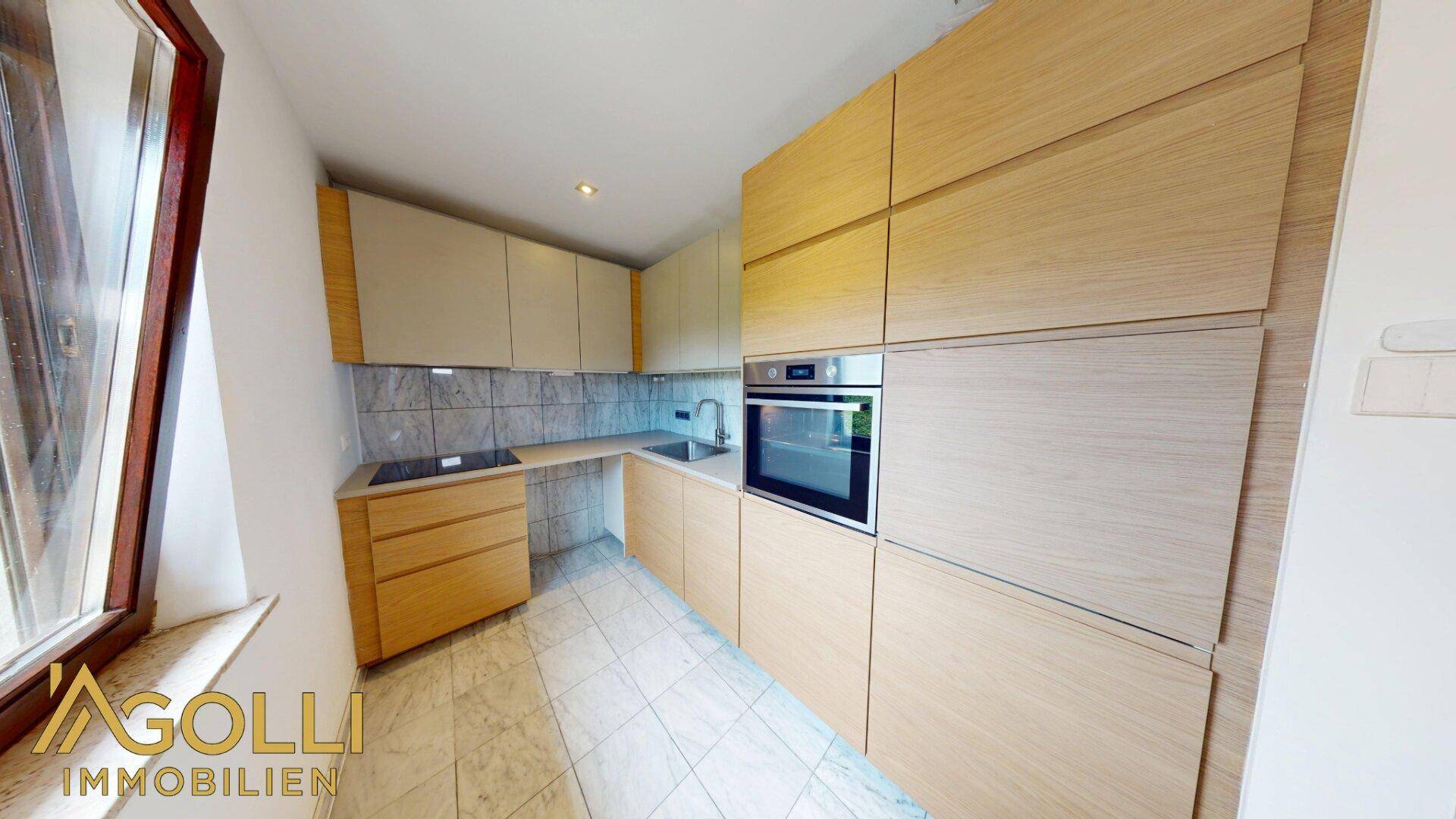 Moderne Einbauküche mit hellen Holzfronten, integrierten Geräten und Fliesenboden.