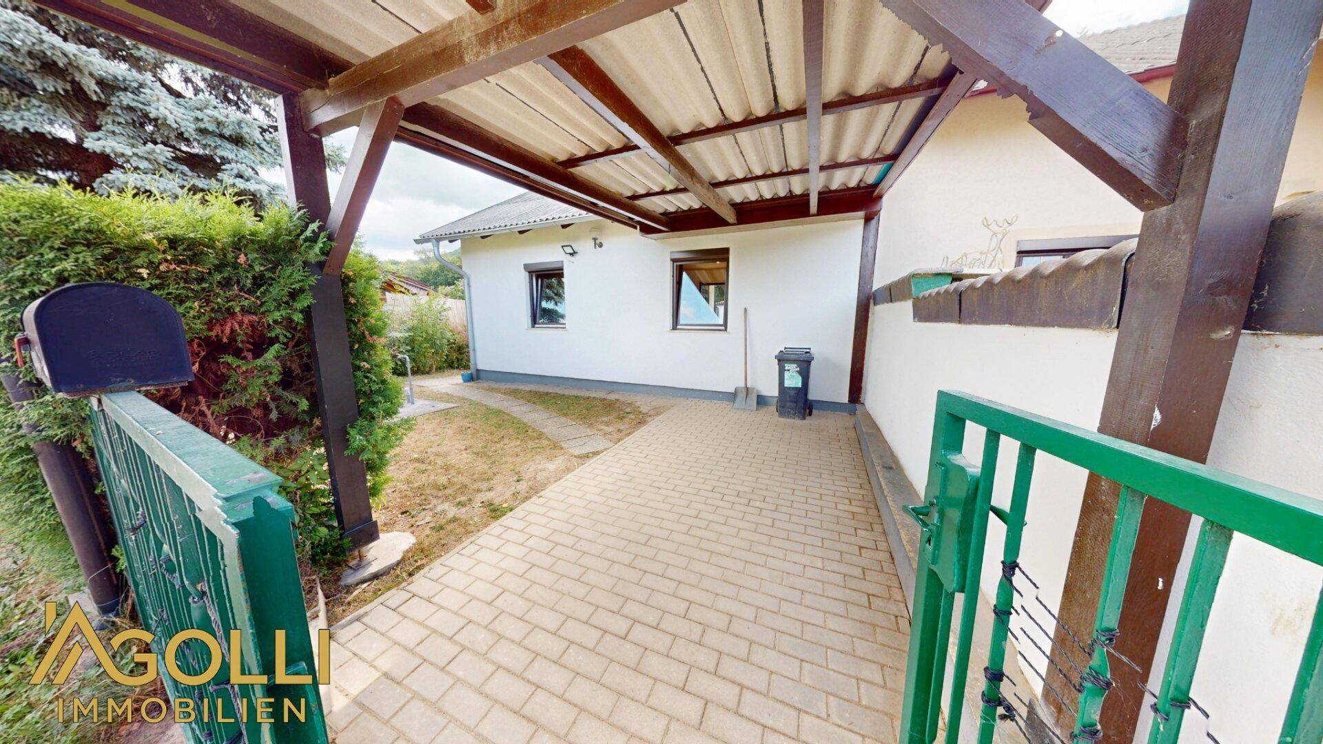 Eingangsbereich mit überdachtem Carport und gepflastertem Weg zum Haus.