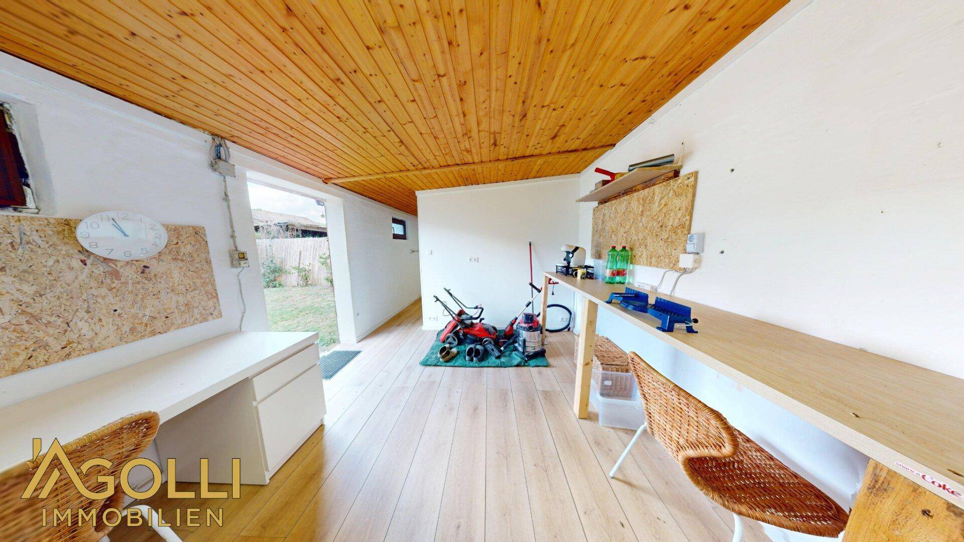 Geräumige Werkstatt im Gartenhaus mit Holzdielenboden, Arbeitsflächen und Zugang zum Garten.