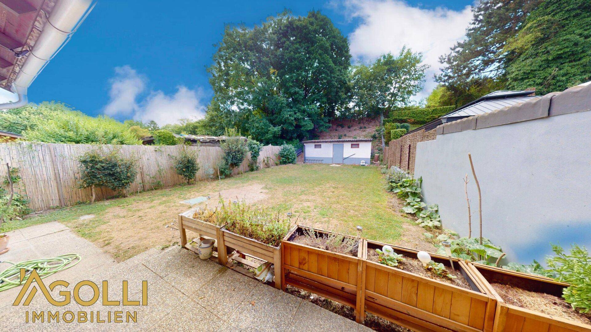 Großer Gartenbereich mit Rasenfläche, erhöhten Pflanzbeeten und umgebender Vegetation.