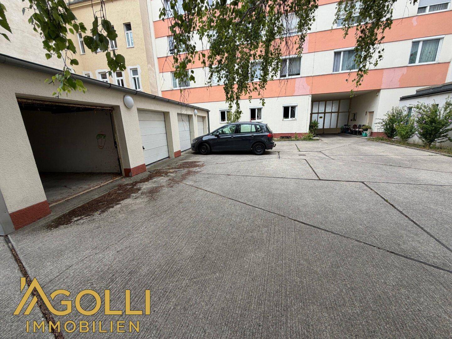 Mehrere Garagen und ein großer Parkplatz vor einem Wohngebäude im Hintergrund.