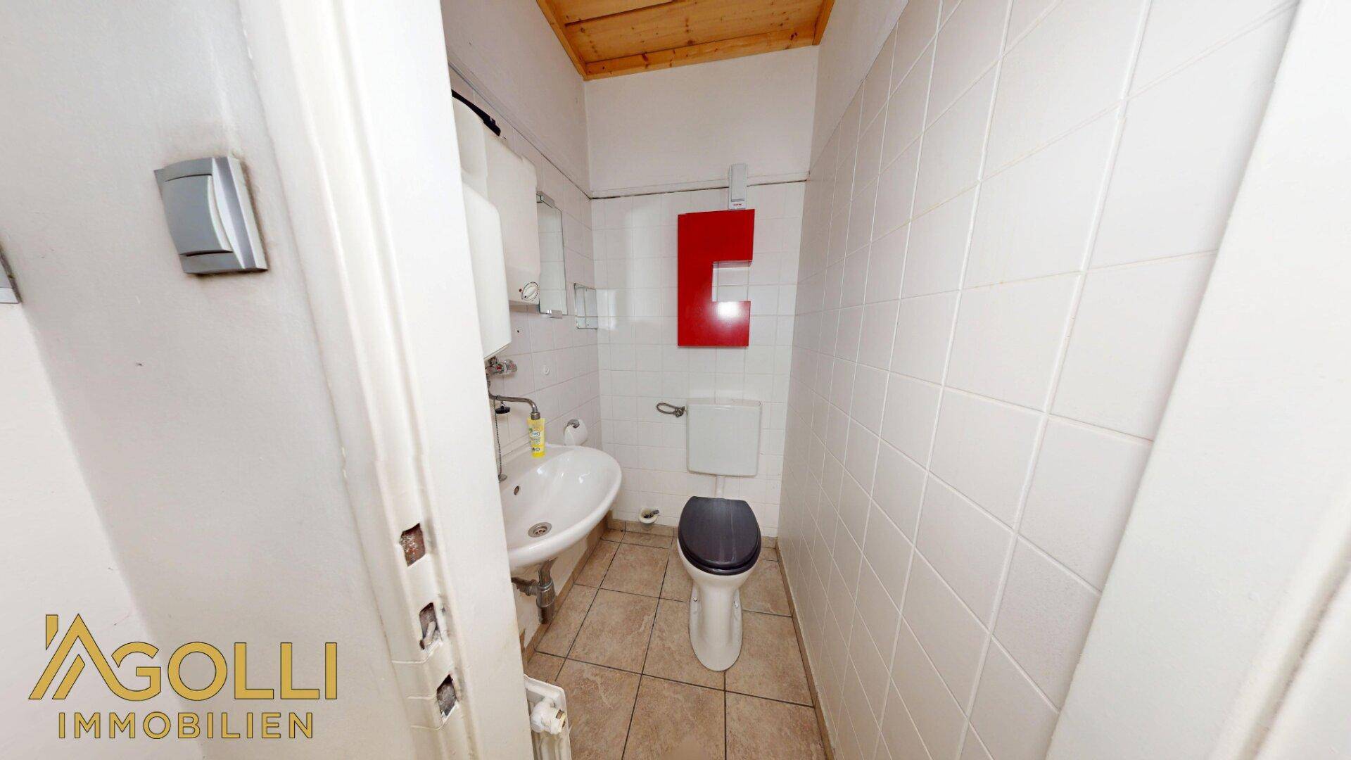 Kleine Toilette mit Waschbecken, WC und weißen Fliesen an den Wänden.