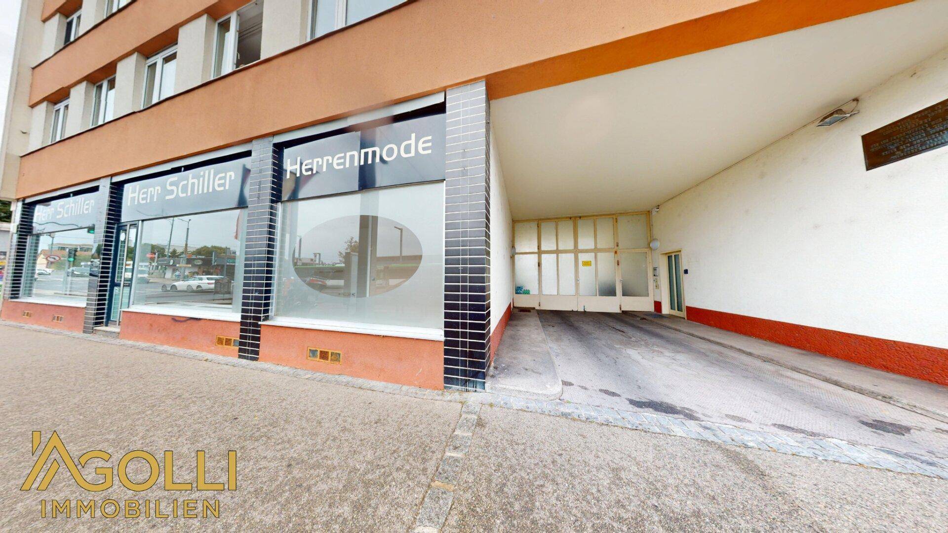 Fassade des Gebäudes mit Ladenfront und Zufahrt zu einer Tiefgarage oder Rampe.