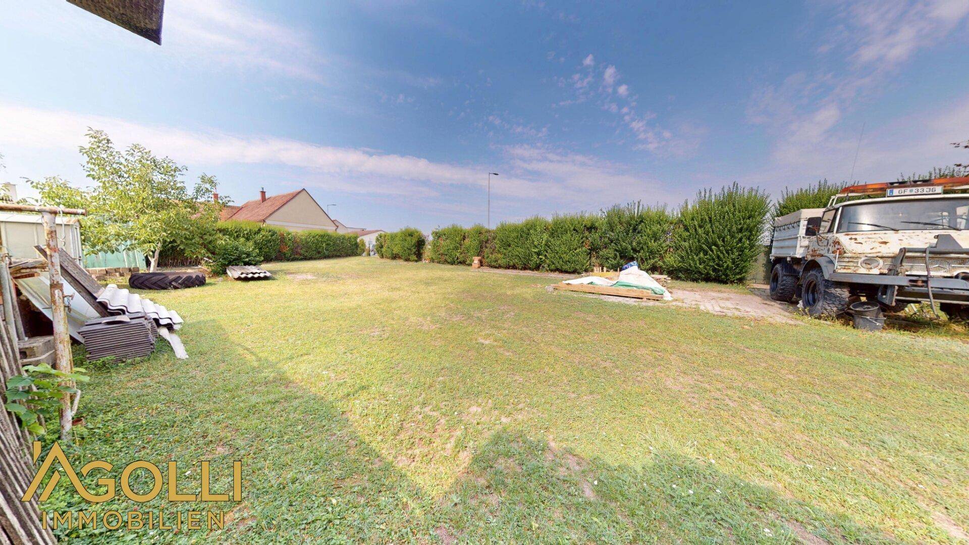 Großer, gepflegter Gartenbereich mit Rasenfläche, Hecke und einem Nutzfahrzeug am Rand.