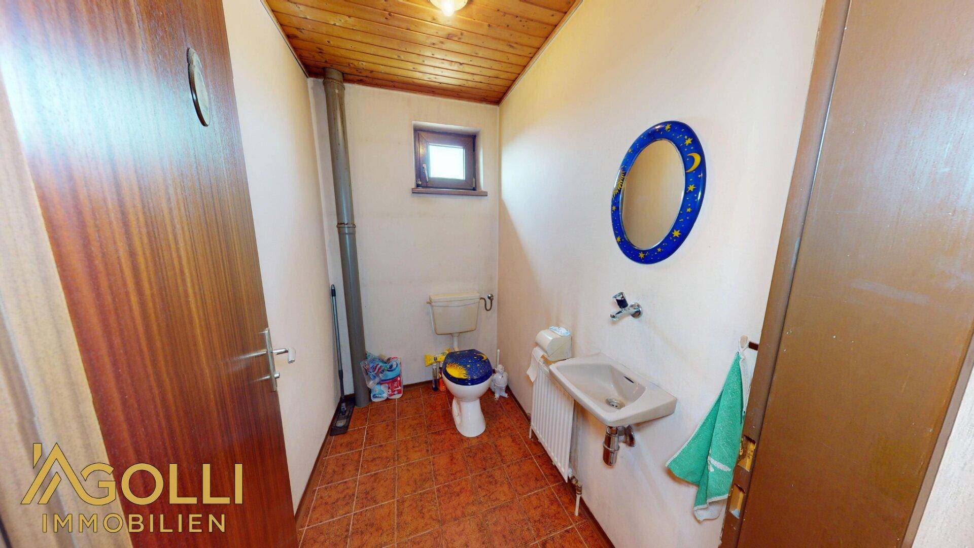 Kleines WC mit Fenster, gefliestem Boden und Holzdecke.