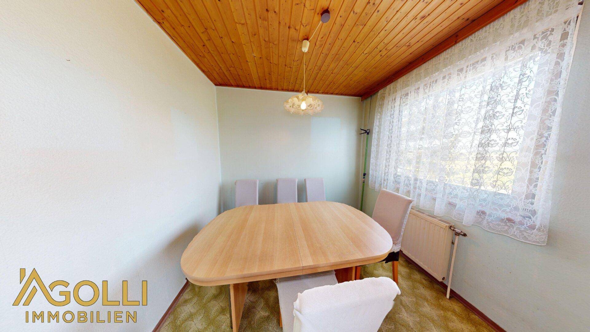 Gemütlicher Essbereich mit Holztisch, Stühlen und einem Fenster mit Vorhängen.