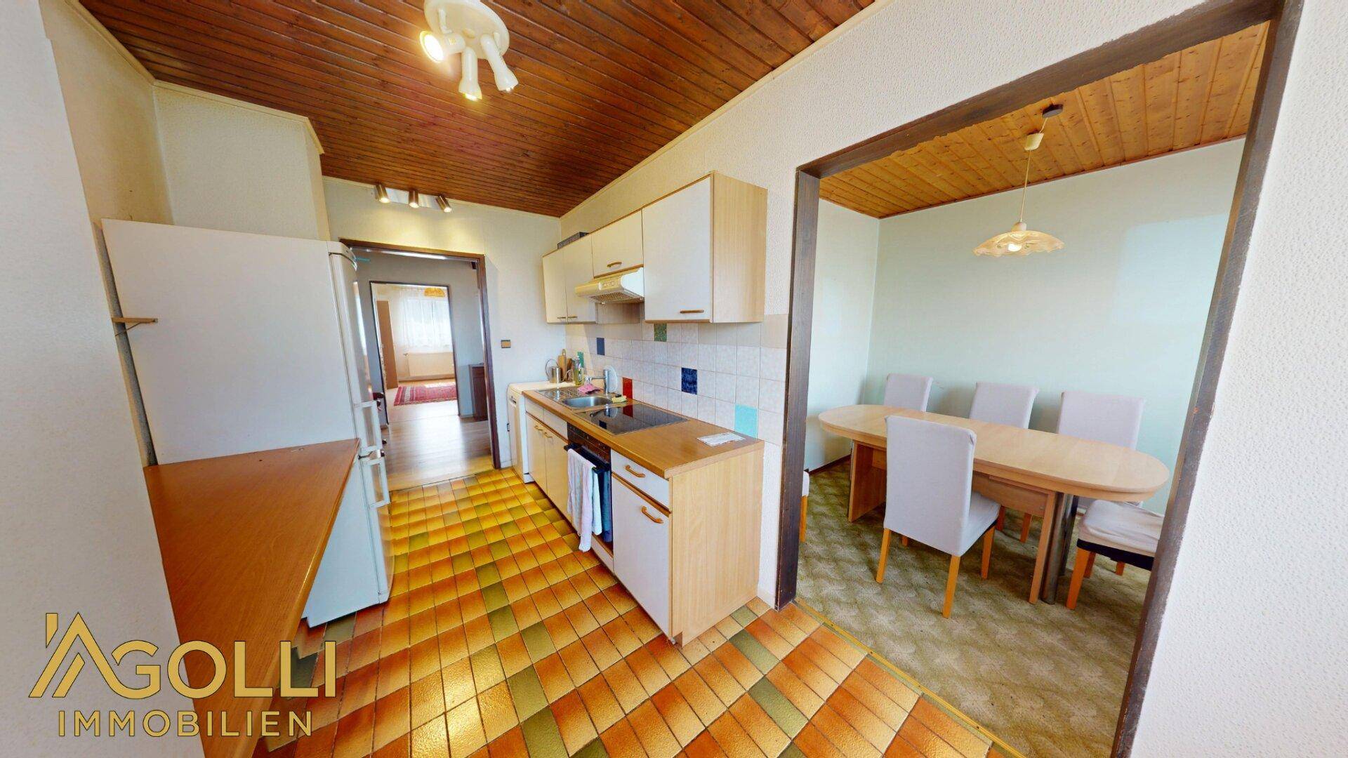 Funktionale Küche mit Holzdecke, gefliestem Boden und angrenzendem Essbereich.