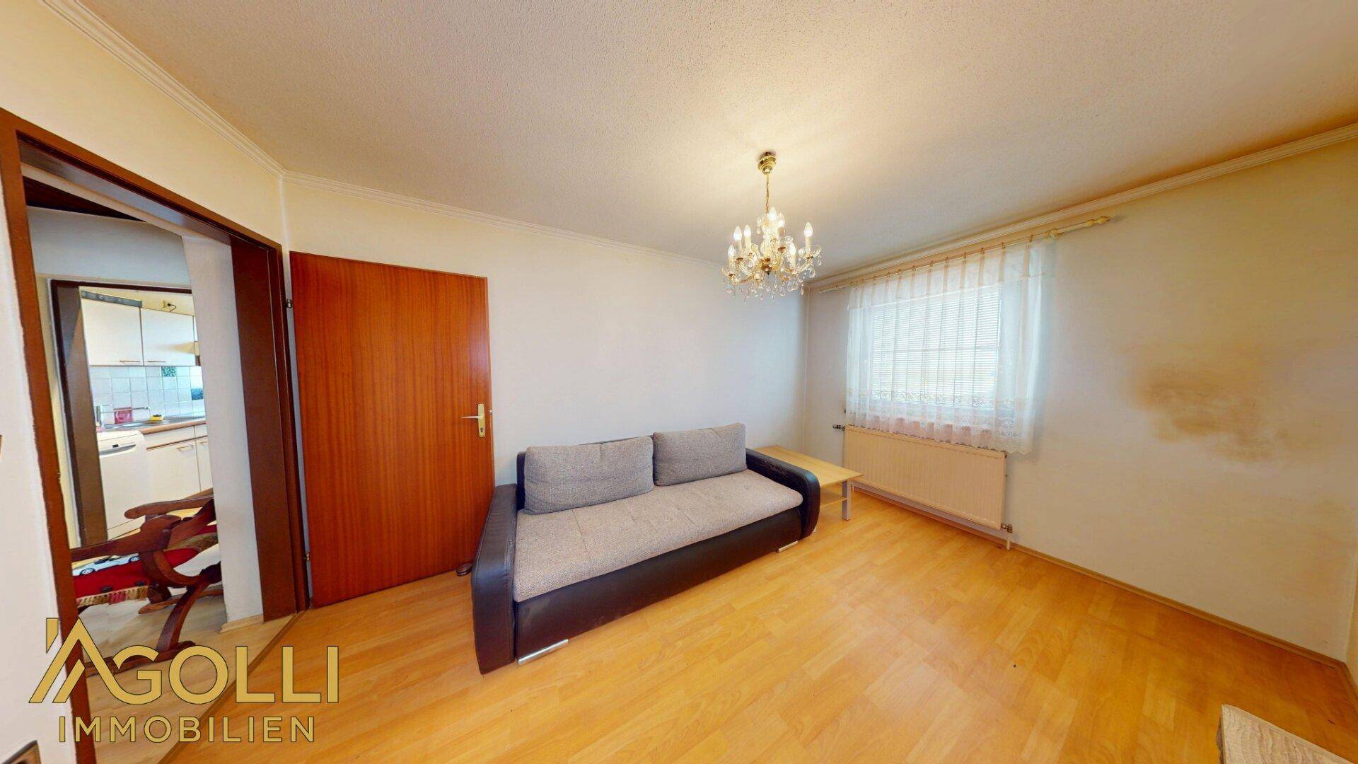 Heller Raum mit Sofa, Holzboden und einem Kronleuchter an der Decke.