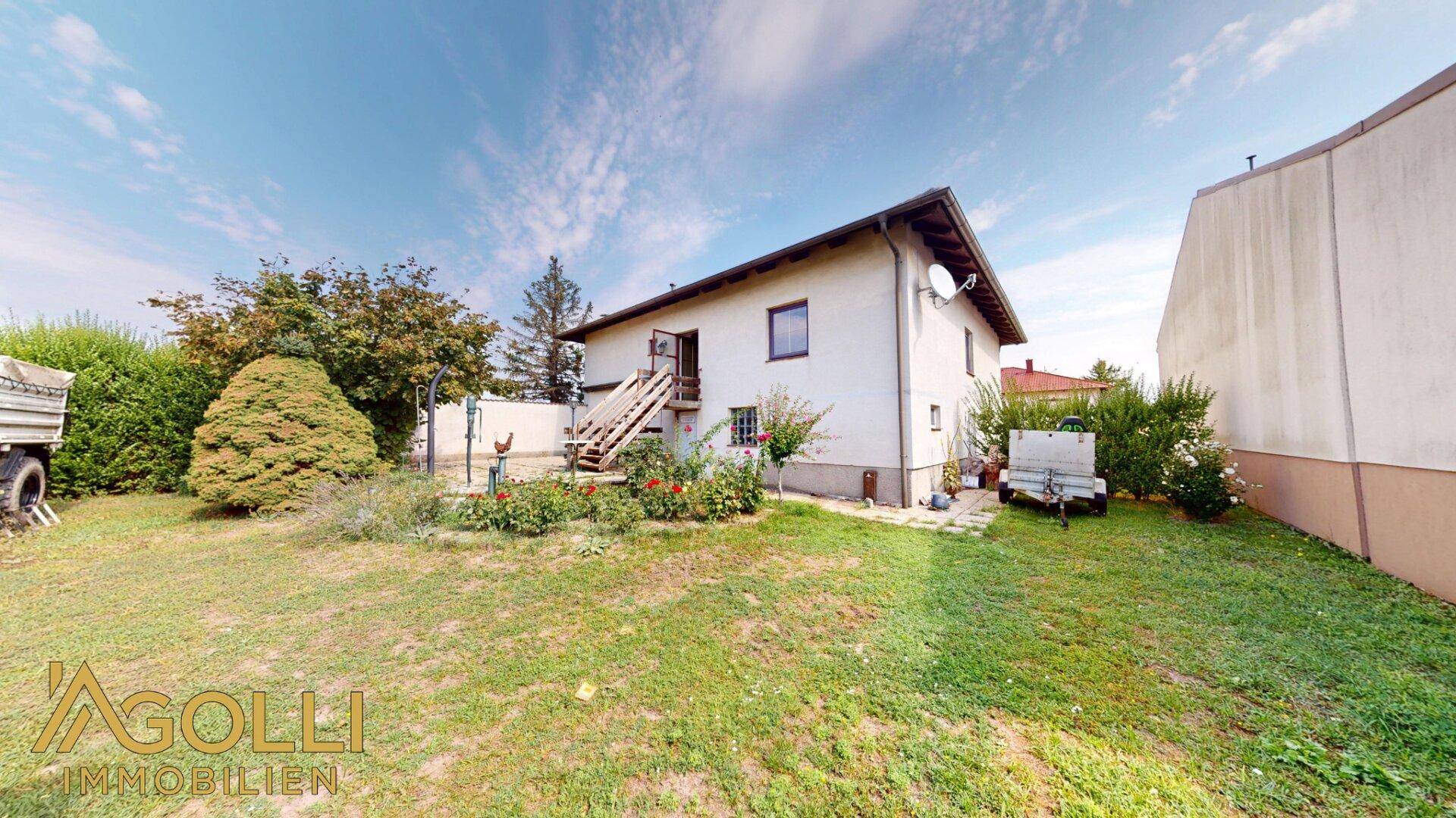 Hinteransicht des Hauses mit Garten, Außentreppe und Blick auf die umliegende Landschaft.