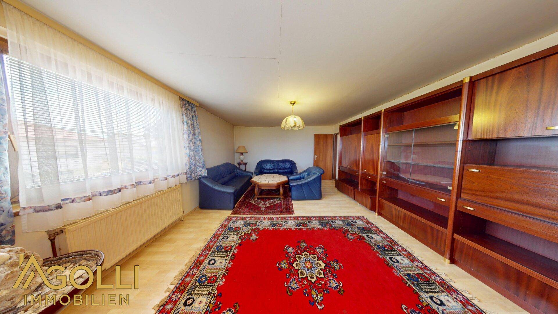 Geräumiges Wohnzimmer mit Laminatboden, großem roten Teppich und Holzregalen.