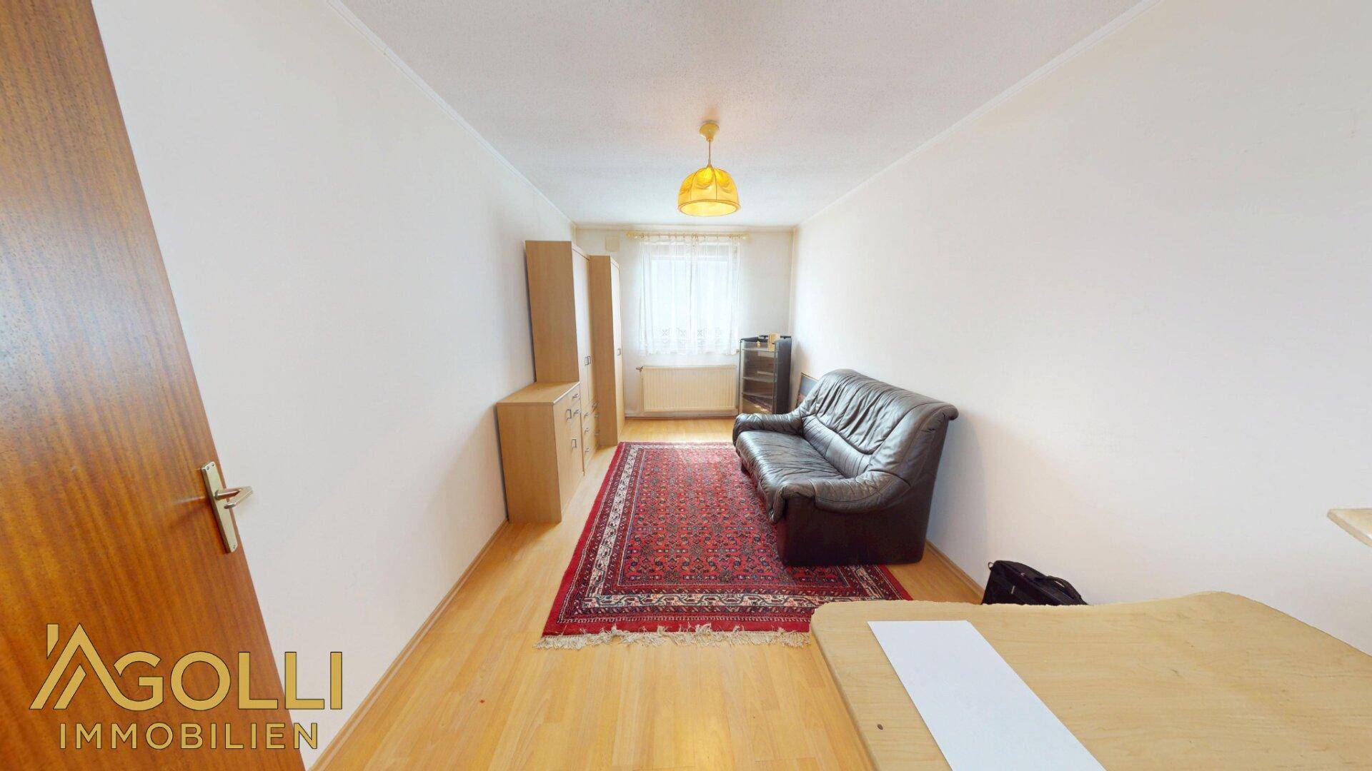 Helles Zimmer mit Ledersofa, Schreibtisch und einem traditionellen Teppich.