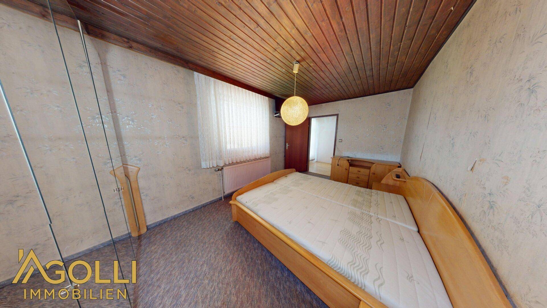 Schlafzimmer mit Holzbett, gemusterter Tapete und einer Holzdecke.
