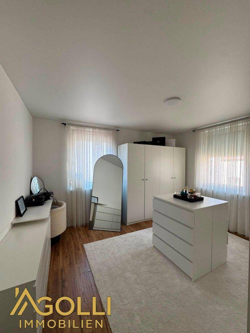 Helles Schlafzimmer mit Holzboden, weißem Kleiderschrank, Kommode und großem Spiegel.