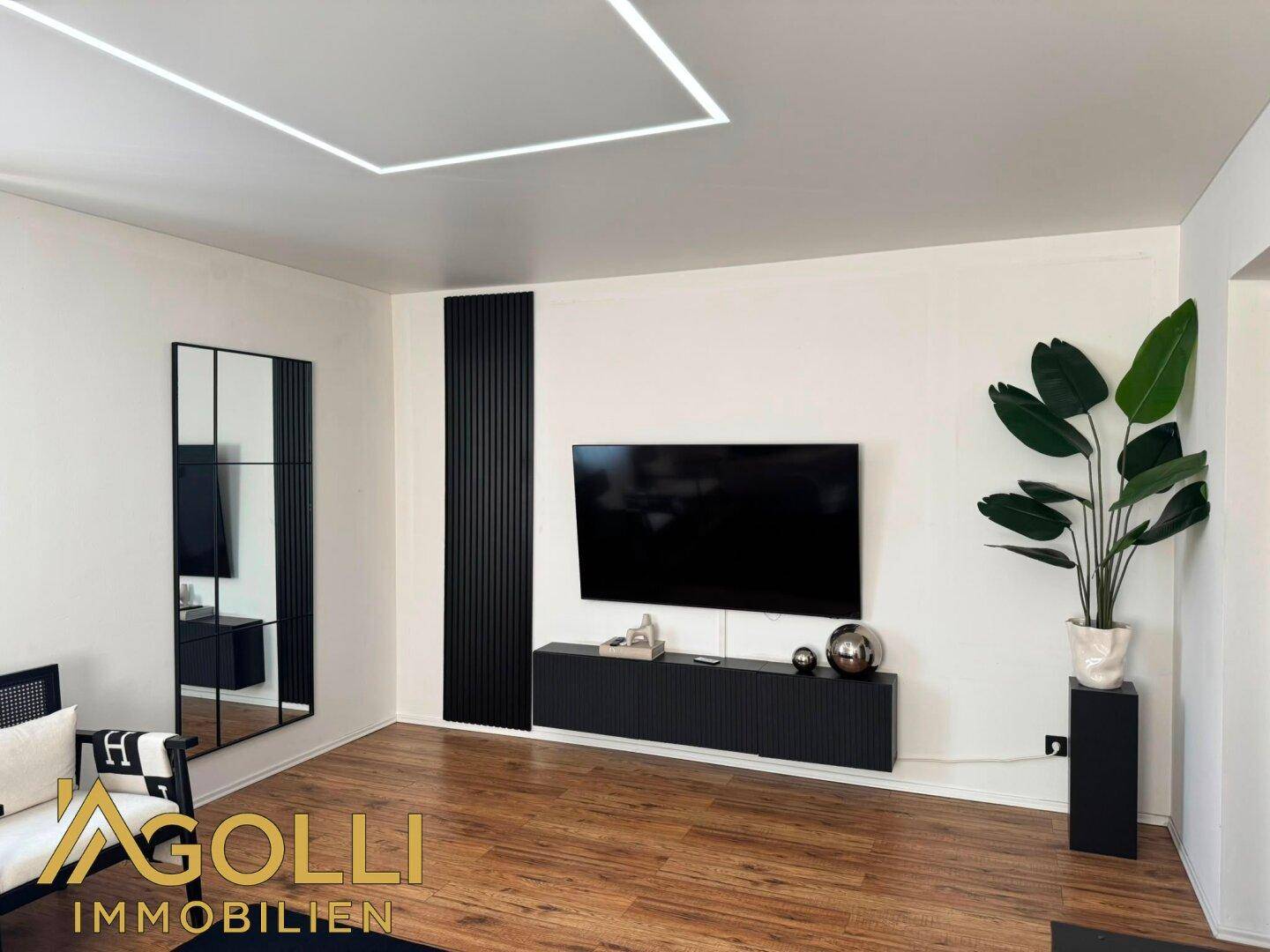 Helles Wohnzimmer mit Holzboden, moderner Einrichtung, Wandpaneelen und Deckenbeleuchtung.