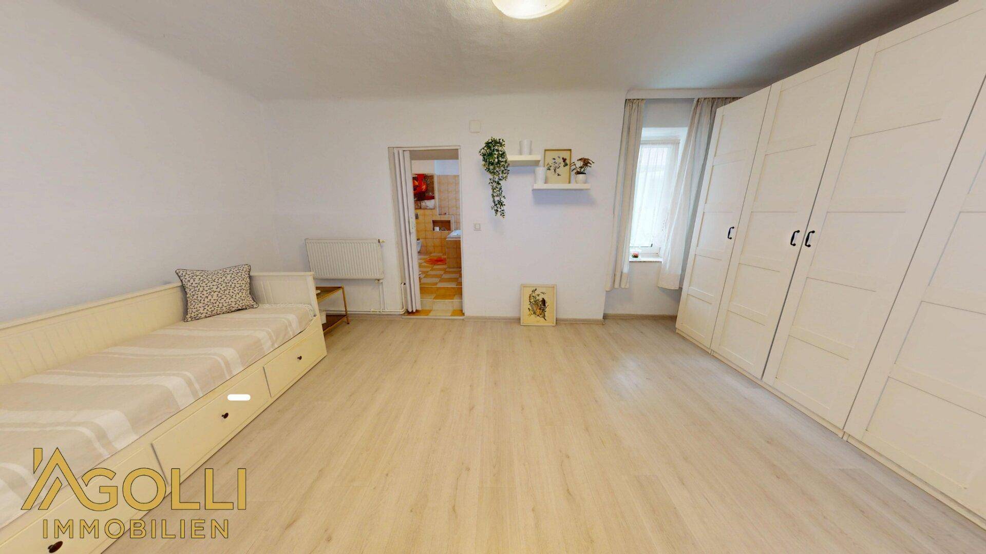 Helles Schlafzimmer mit Laminatboden, Einzelbett und großen weißen Kleiderschränken.