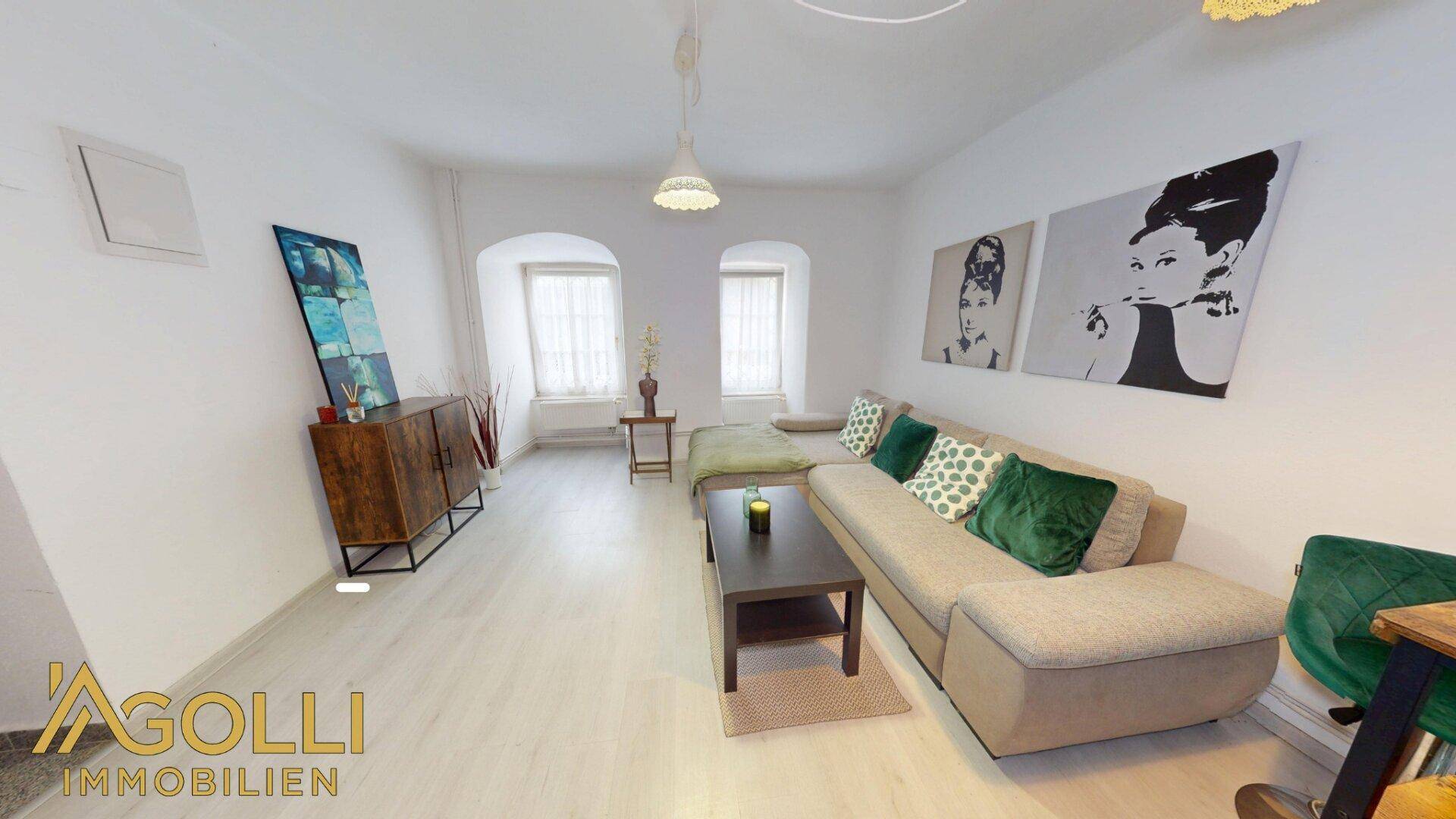 Gemütliches Wohnzimmer mit hellem Laminatboden, Sofa und dekorativen Bildern an der Wand.