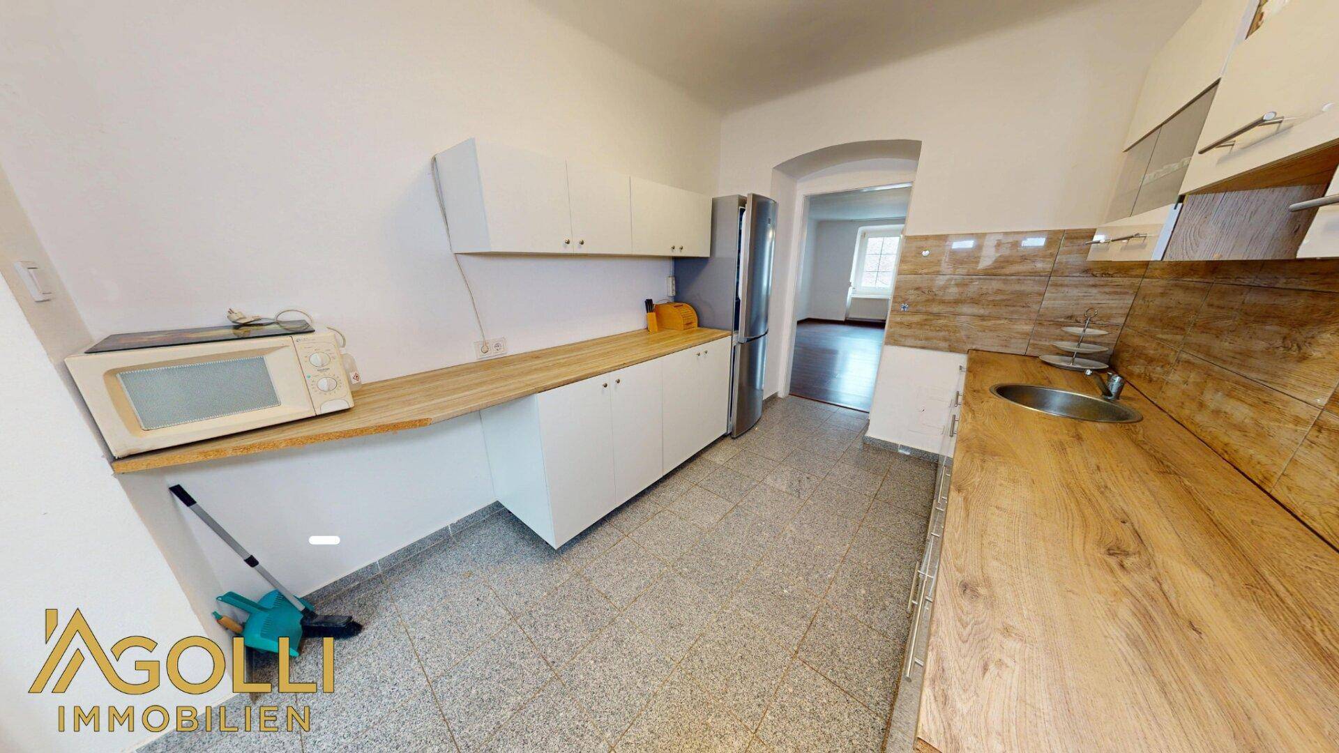 Funktionale Küche mit weißen Schränken, Holzarbeitsplatten und gefliestem Boden.