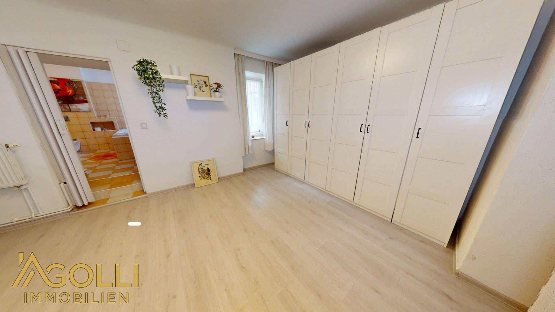 Geräumiges Schlafzimmer mit Laminatboden und einer Reihe von weißen Kleiderschränken.