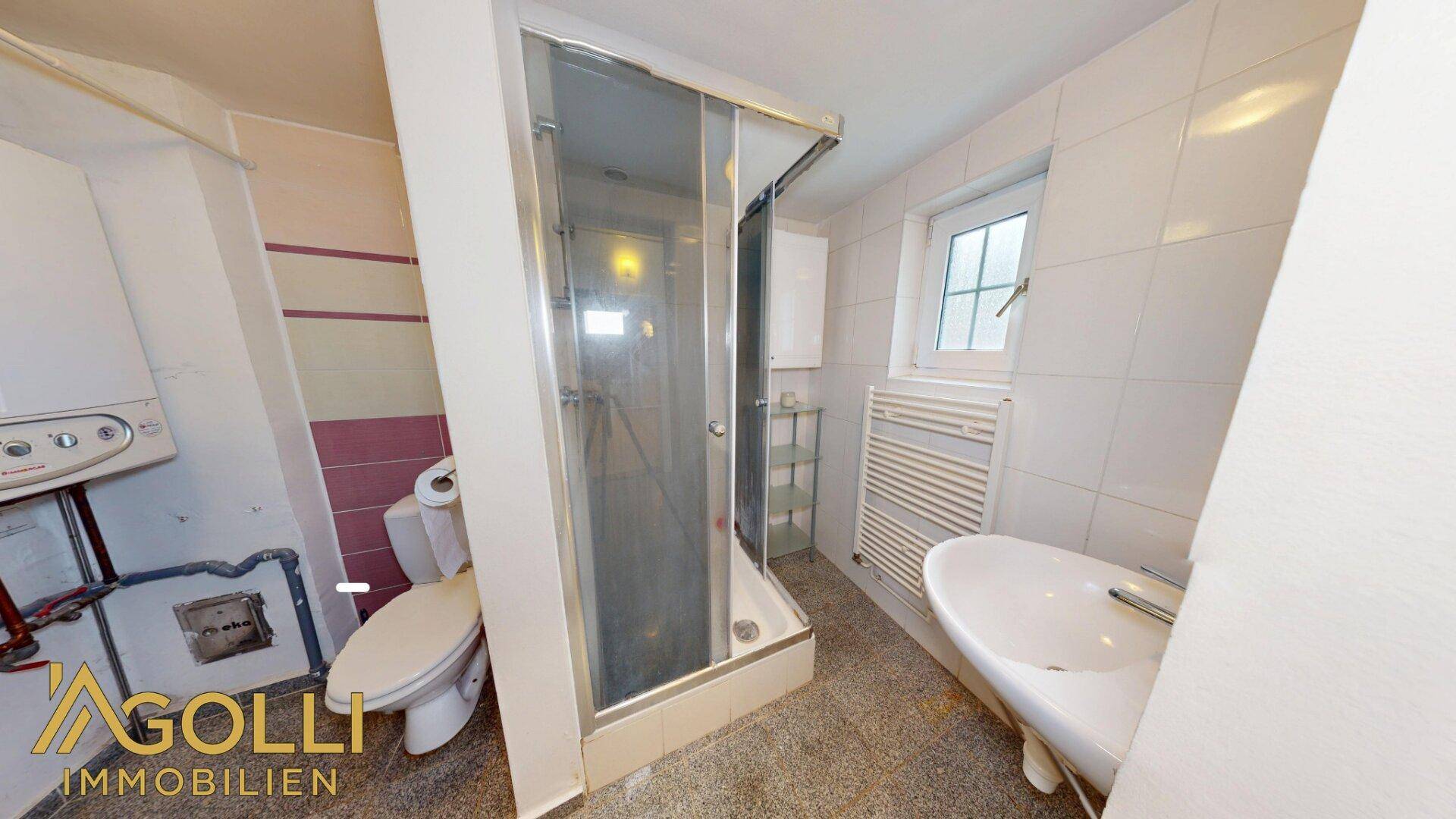 Kleines Badezimmer mit Dusche, WC und Heizungsanlage, funktional eingerichtet.