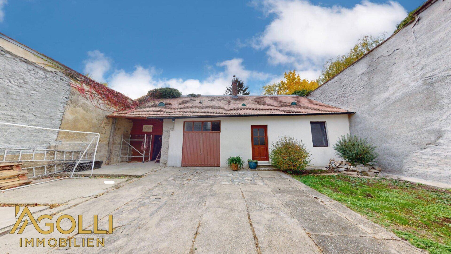 Hinterhof mit Garage und gepflasterter Fläche, umgeben von alten Mauern.