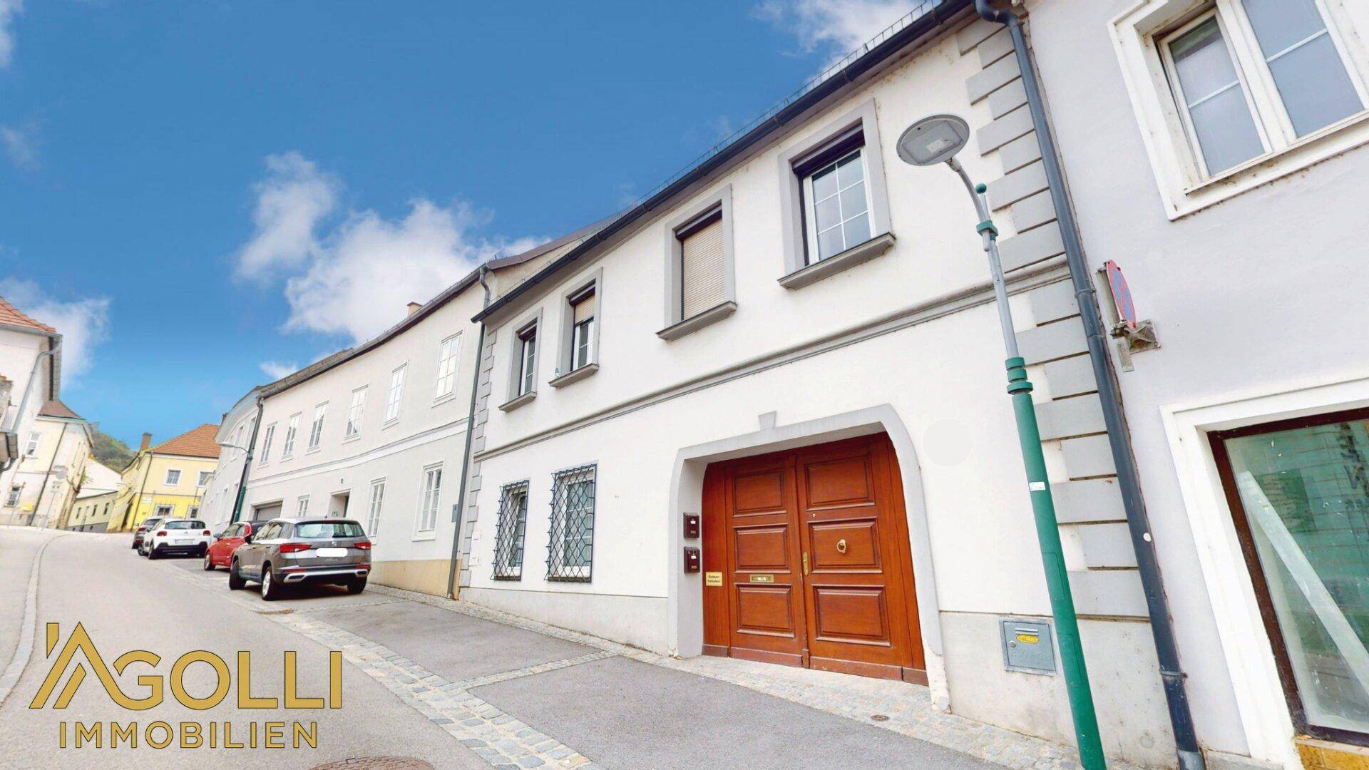 Historisches Stadthaus mit gepflasterter Straße und parkenden Autos in der Umgebung.