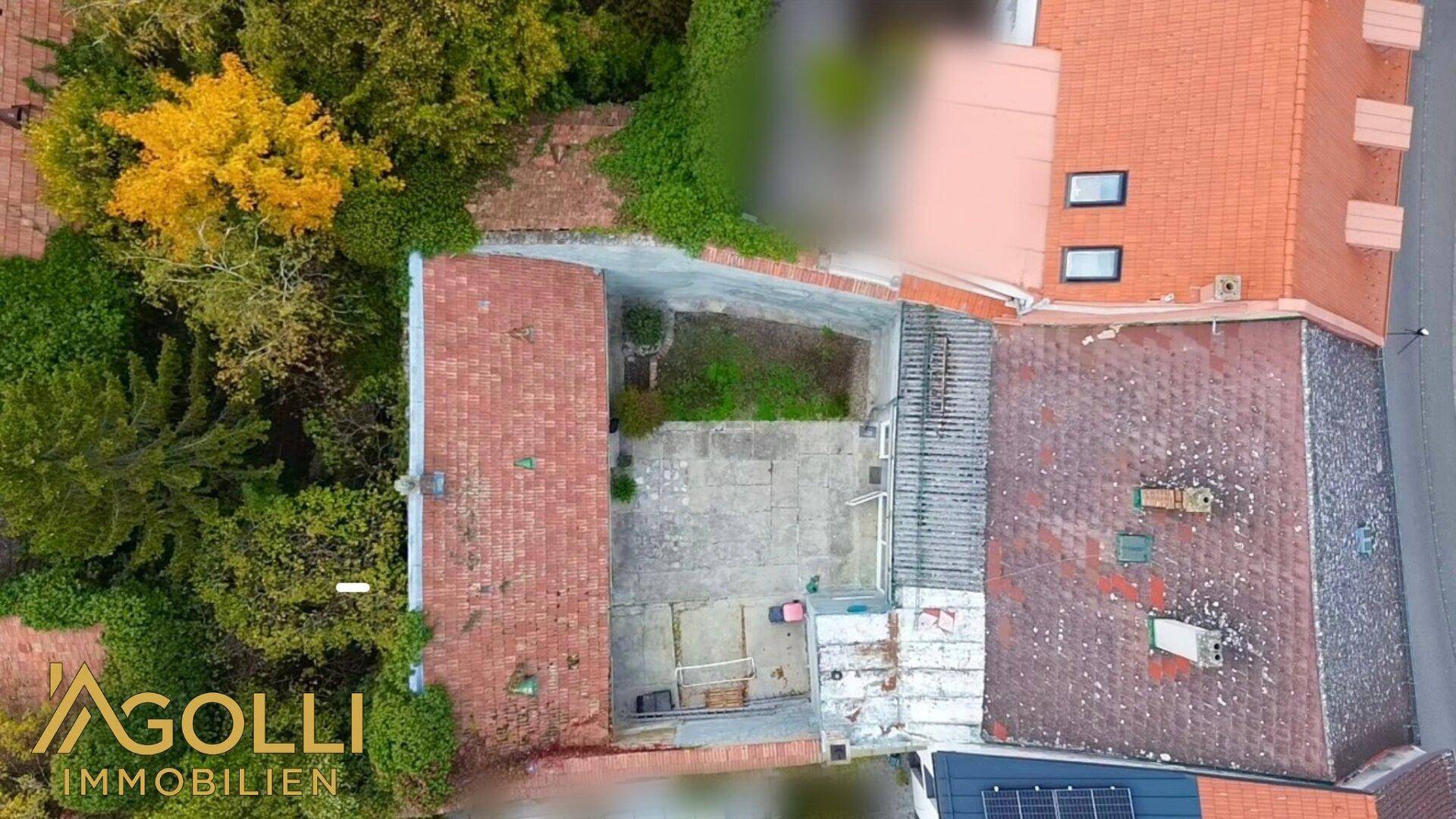 Draufsicht des Grundstücks mit Innenhof, umgeben von Bäumen und Dächern.