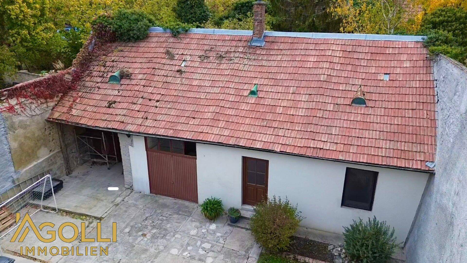 Hinterhofansicht mit Garage, gepflastertem Bereich und altem Ziegeldach.