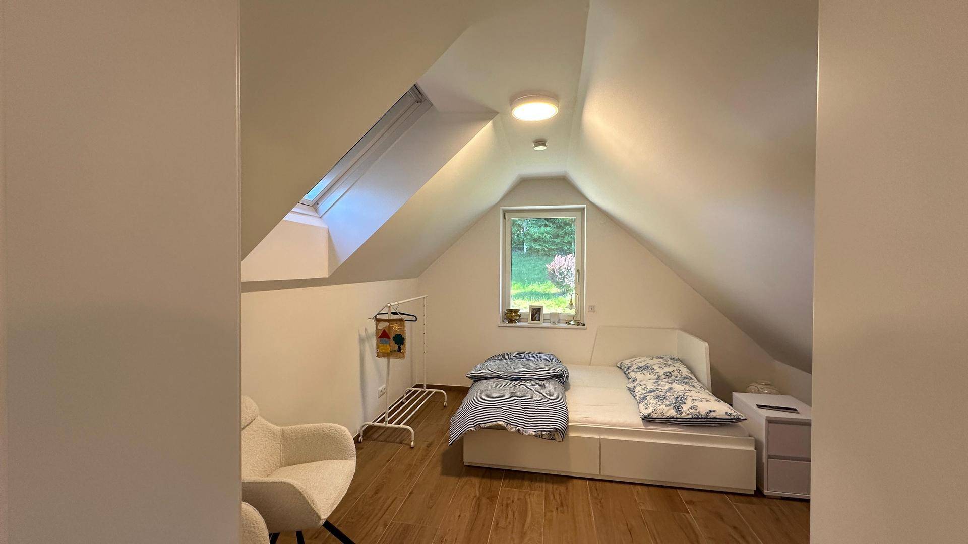 Helles Schlafzimmer im Dachgeschoss mit Dachschräge, Holzboden und Blick ins Grüne.