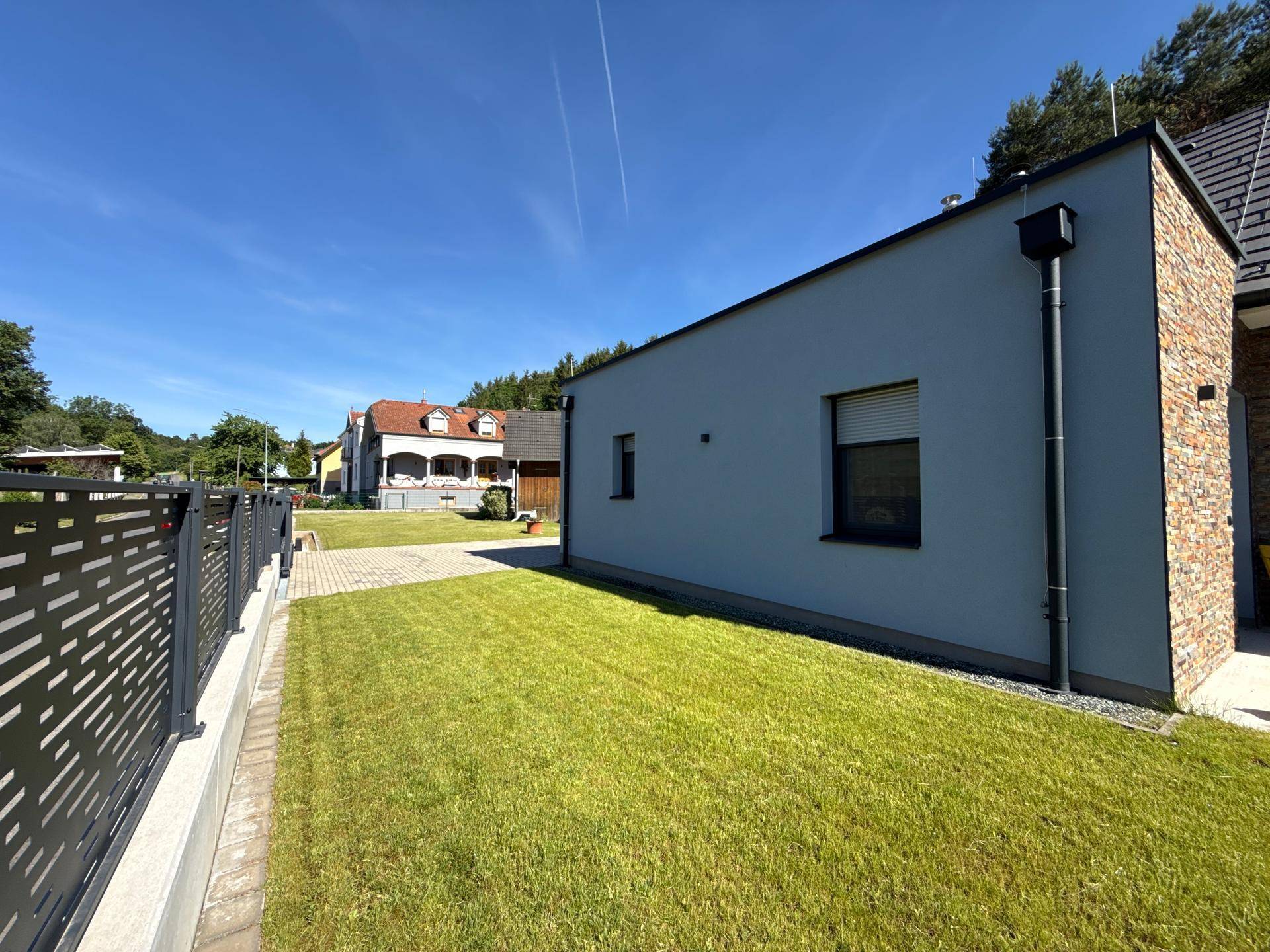 Moderne Hausfassade mit Rasenfläche und gepflasterter Zufahrt, umgeben von einem Zaun.