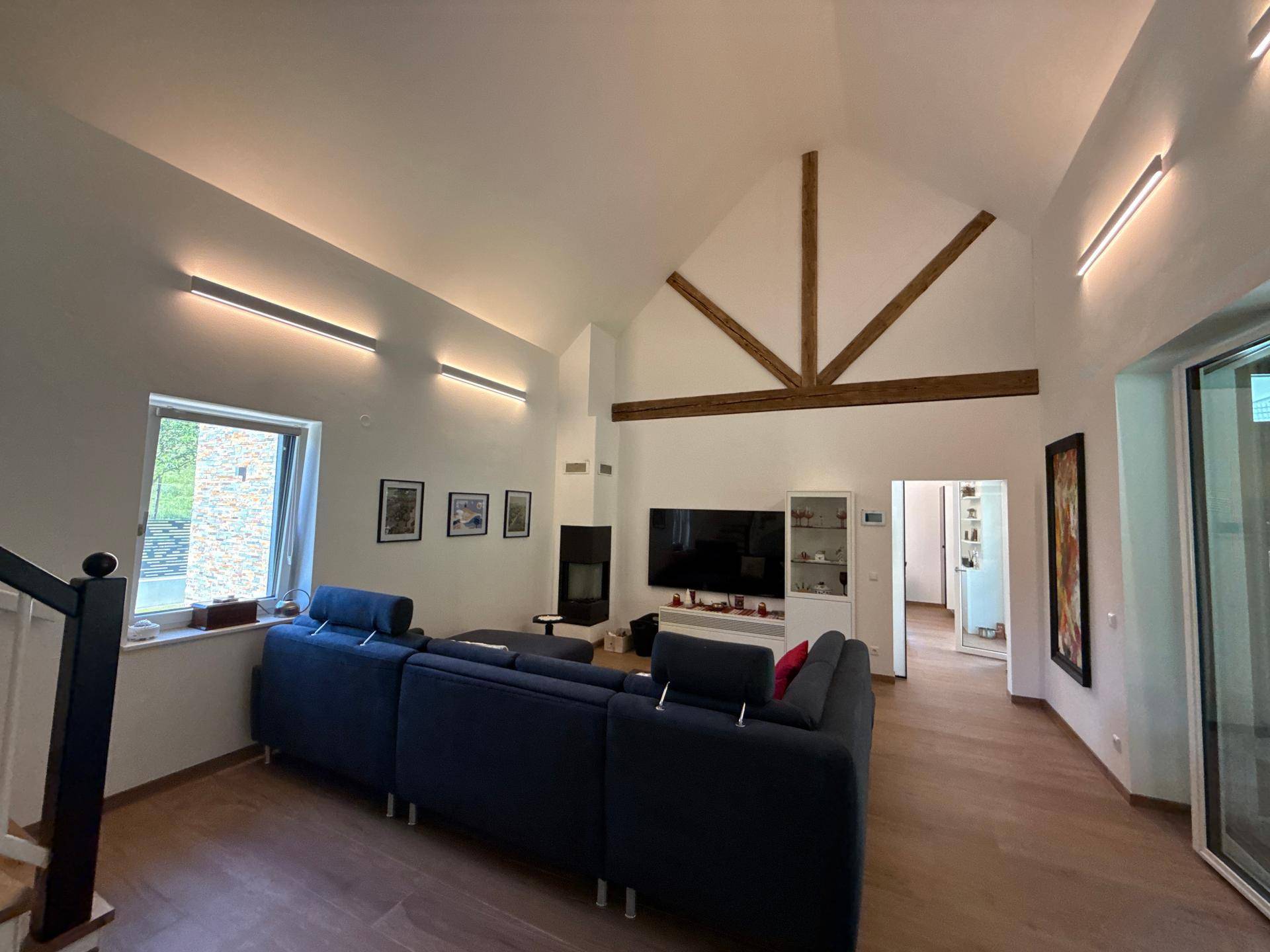 Helles Wohnzimmer mit großem Sofa, Kamin und Blick auf die Treppe und den Außenbereich.