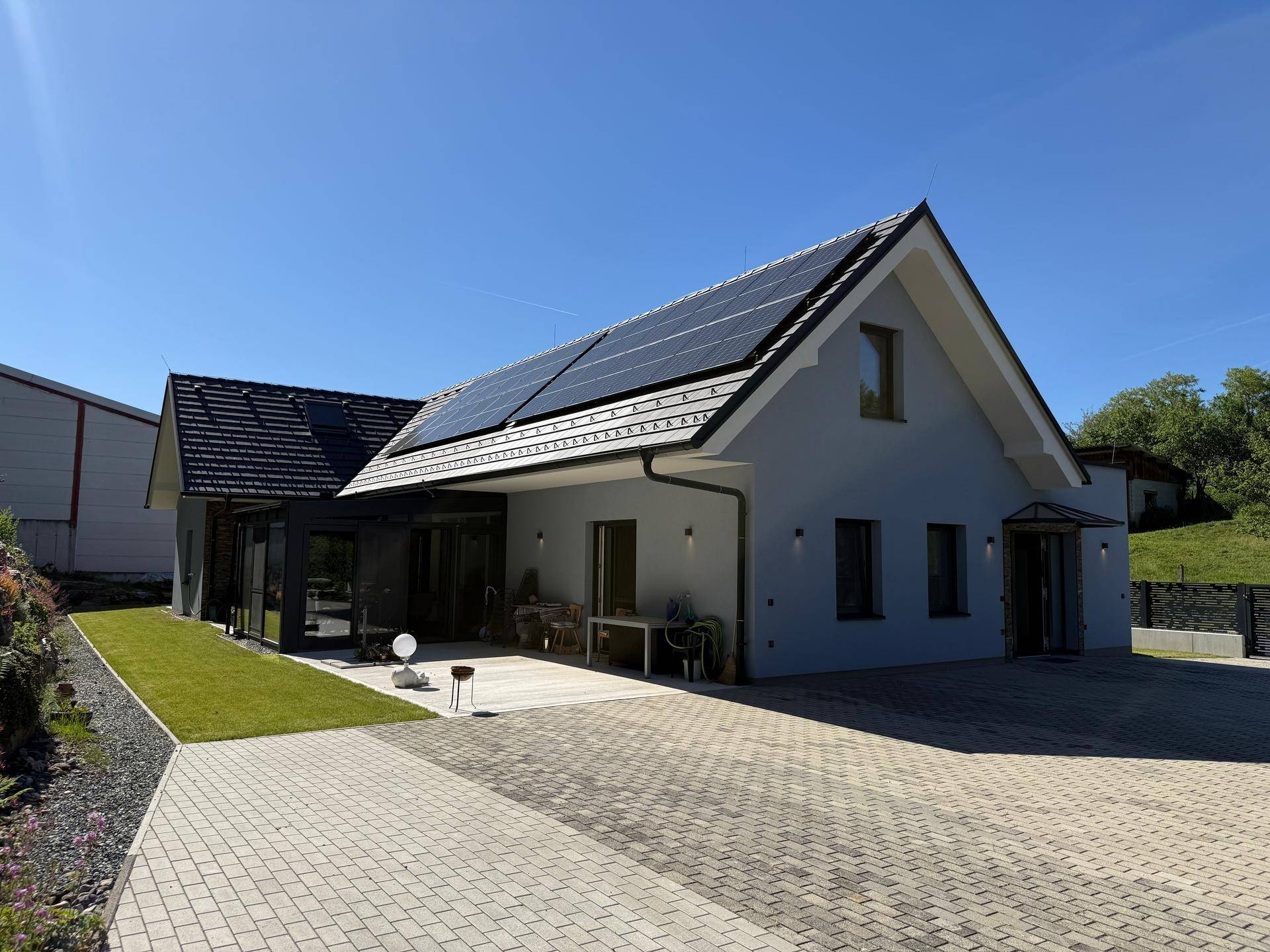 Modernes Einfamilienhaus mit Solaranlage auf dem Dach, gepflasterter Zufahrt und Garten.