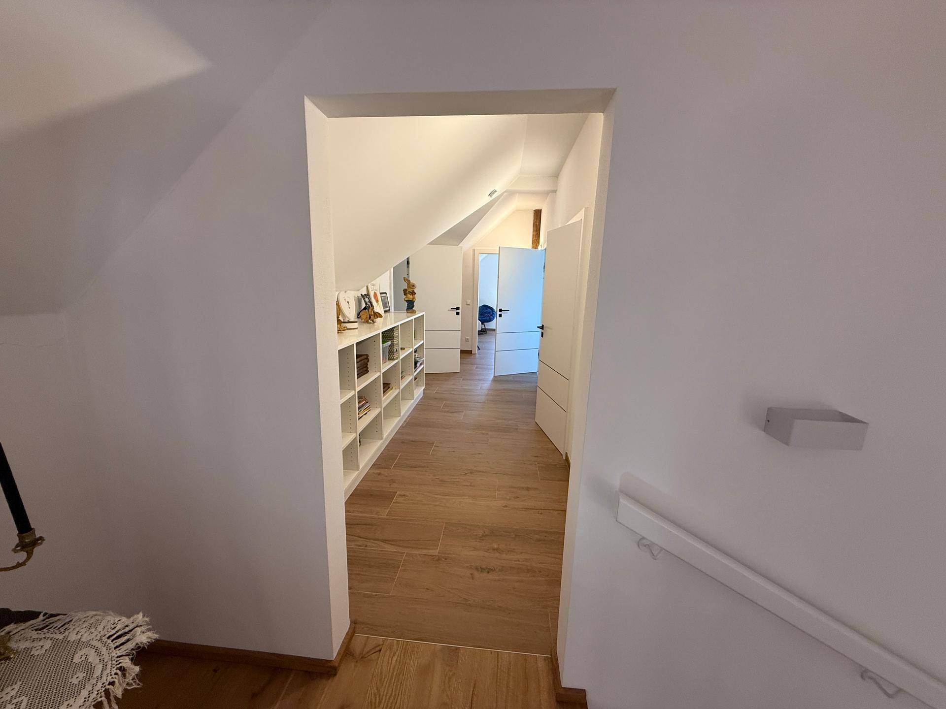 Langer Flur im Dachgeschoss mit Holzboden, Einbauregalen und mehreren Türen.