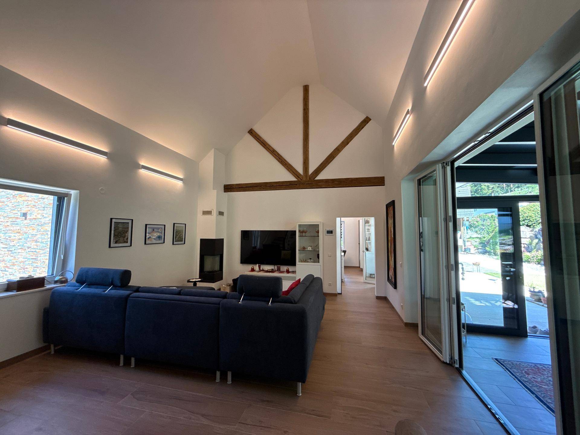 Weitläufiges Wohnzimmer mit hohen Decken, Holzbalken und Zugang zum Außenbereich.