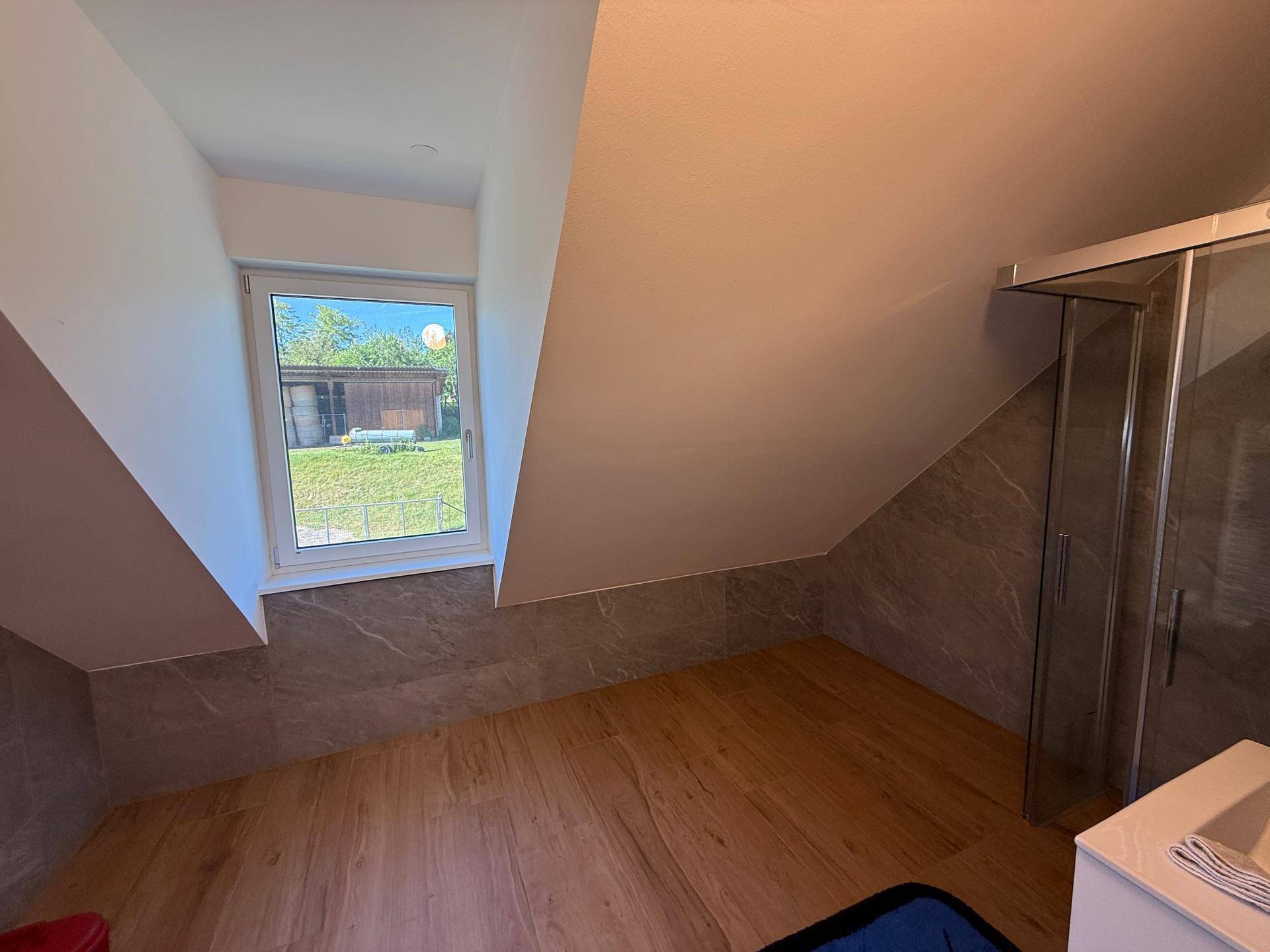 Badezimmer im Dachgeschoss mit Schrägdach, Dusche und Fenster mit Blick ins Grüne.