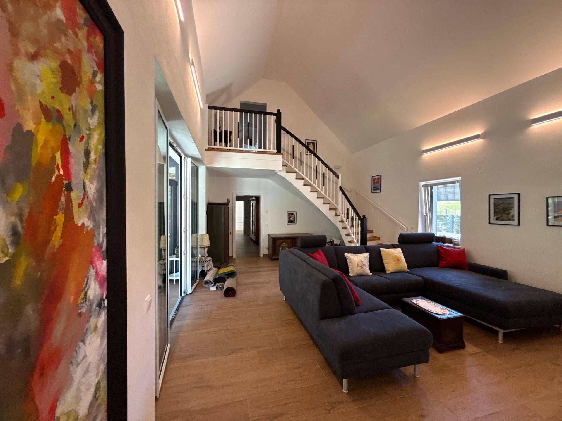 Geräumiges Wohnzimmer mit großem Sofa, Kunstwerk und Blick auf die Treppe und den Essbereich.