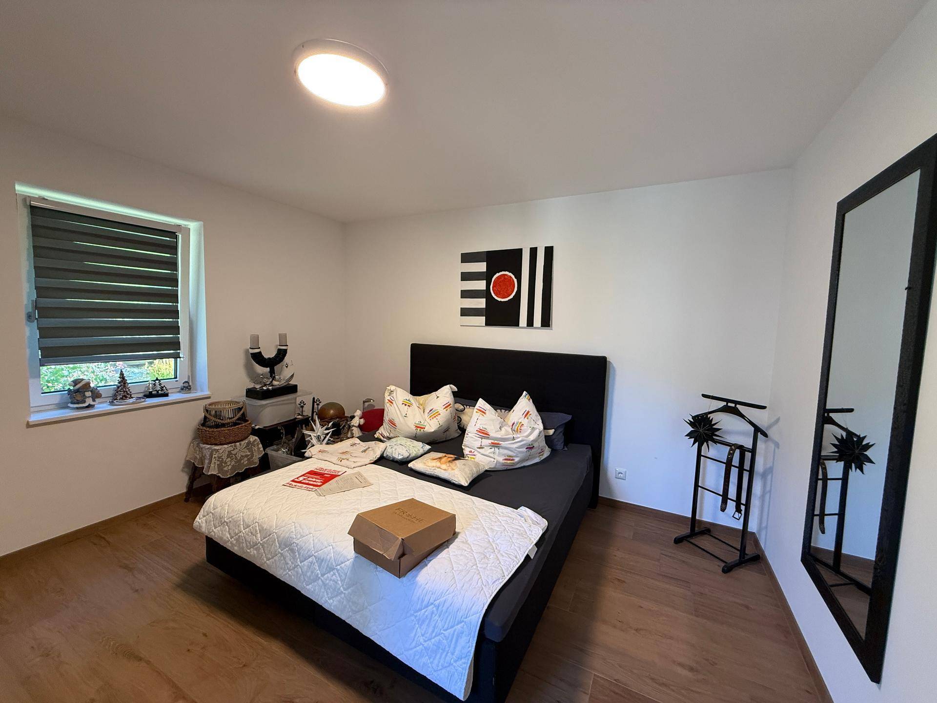 Helles Schlafzimmer mit Doppelbett, Holzboden und Fenster mit Blick ins Grüne.