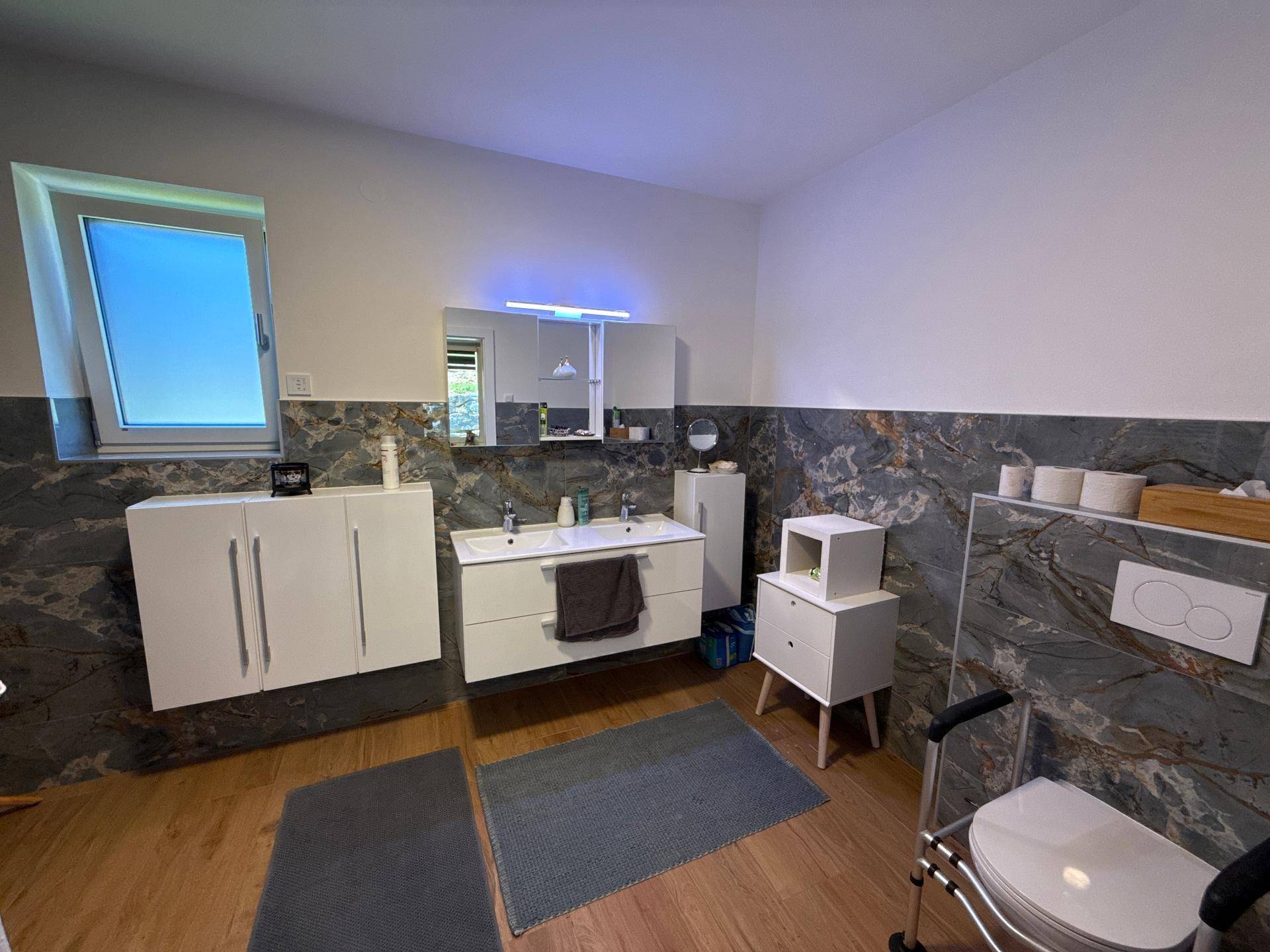Geräumiges Badezimmer mit Doppelwaschbecken, modernen Fliesen und Fenster für Tageslicht.