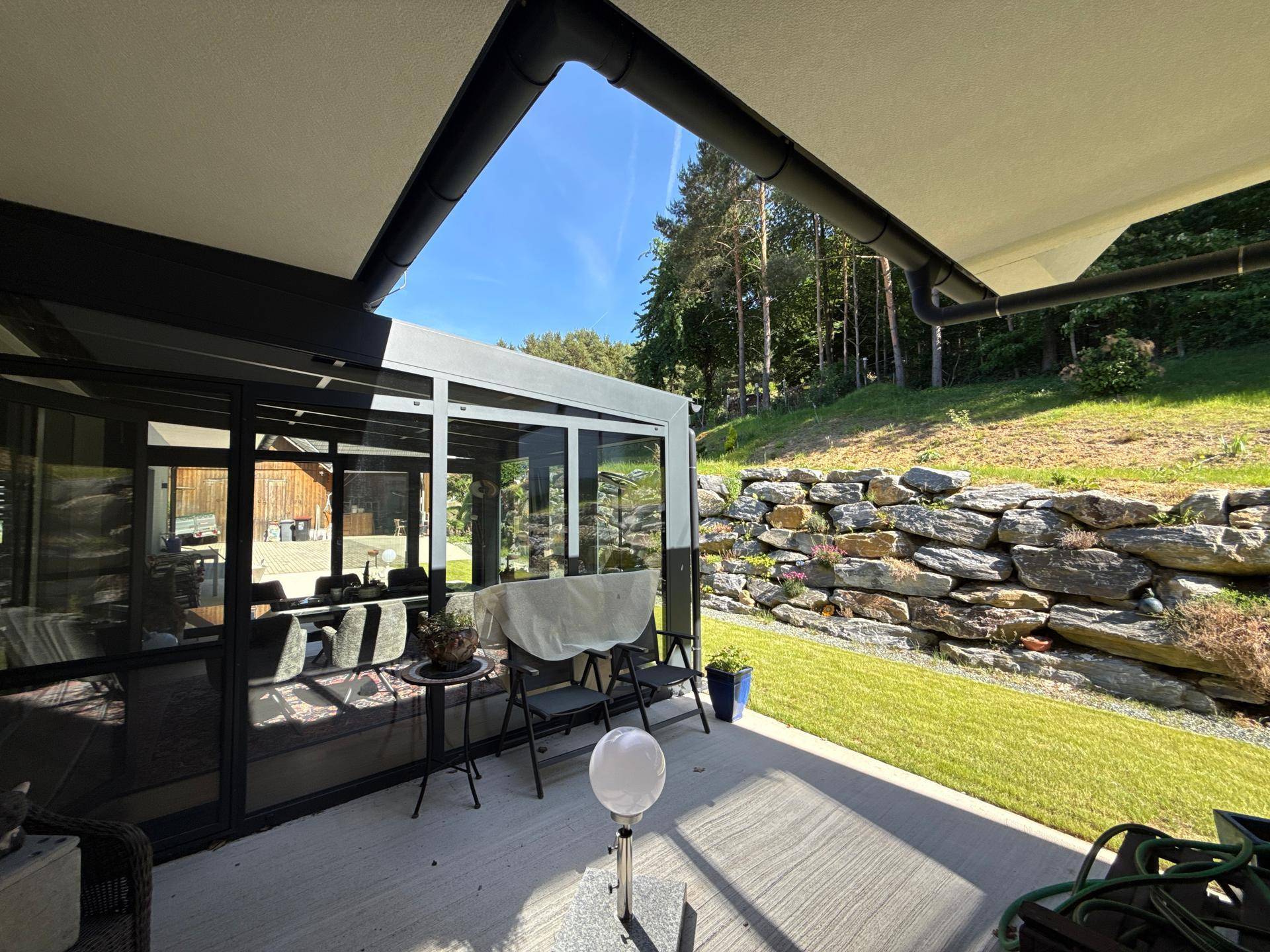 Sonniger Terrassenbereich mit kleiner Sitzgruppe und Blick auf den Garten und die Felswand.