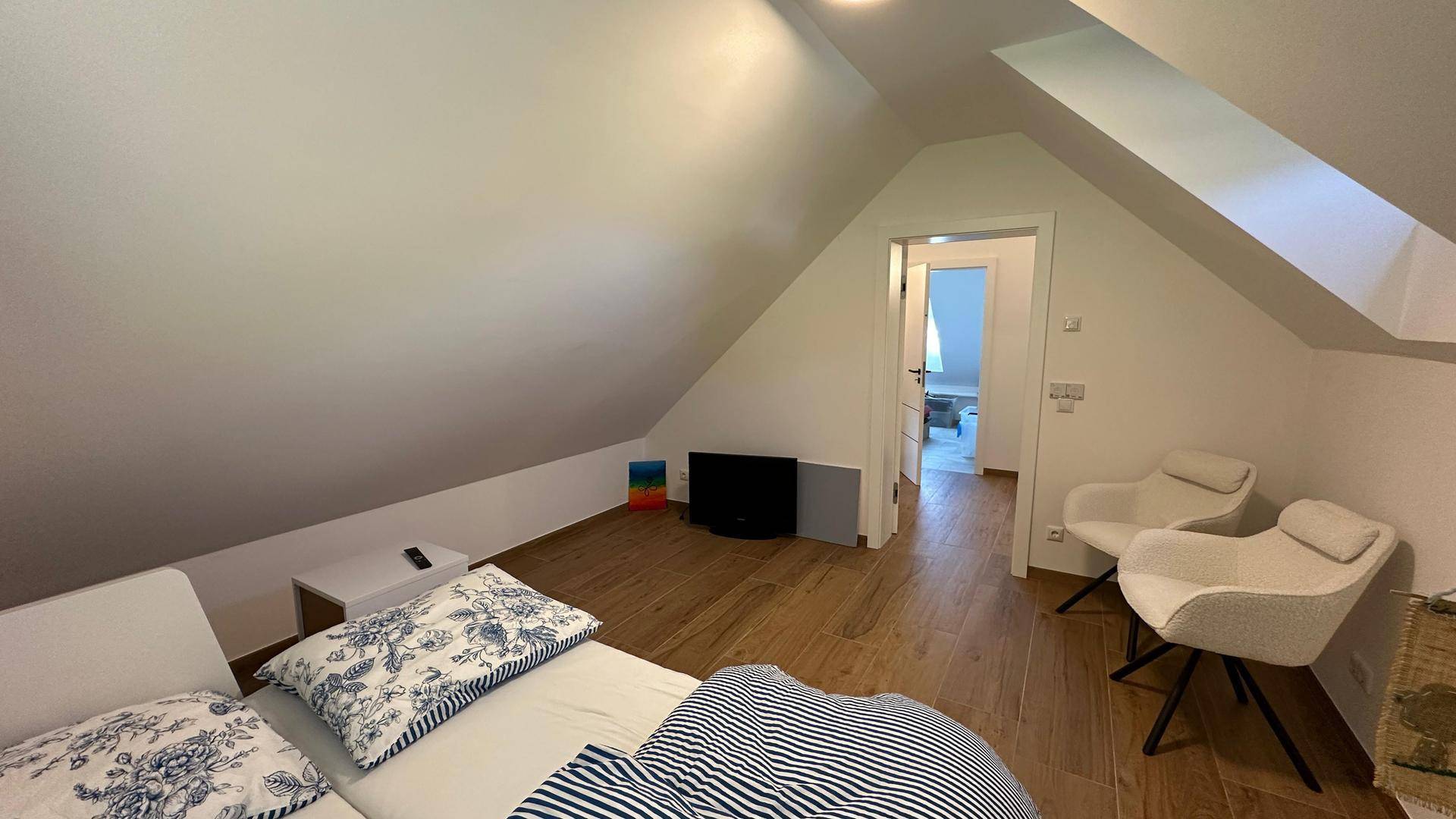 Geräumiges Schlafzimmer im Dachgeschoss mit Holzboden, Dachschräge und Zugang zu weiteren Räumen.