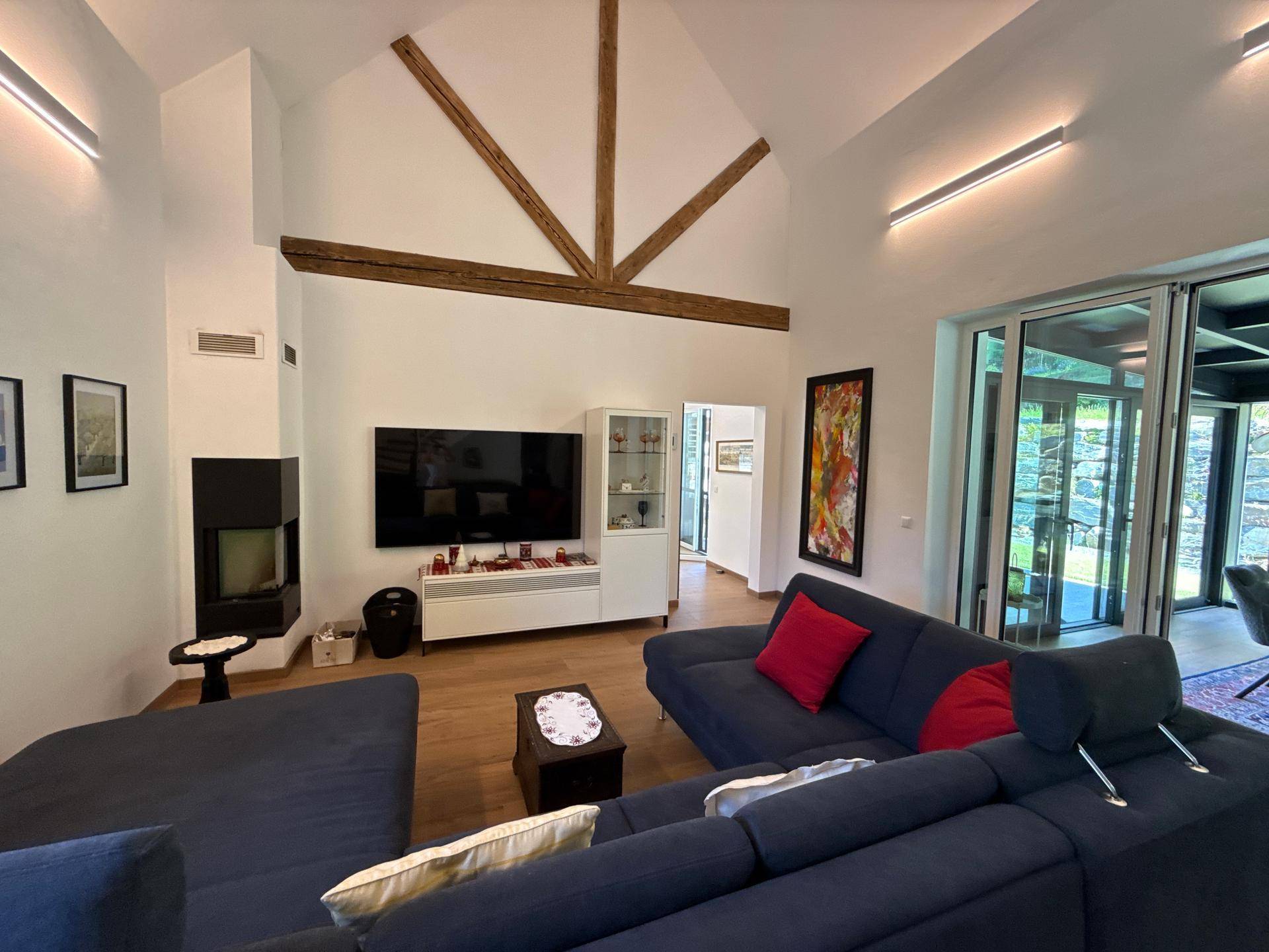 Gemütliches Wohnzimmer mit großem Sofa, Kamin und hohen Decken mit Holzbalken.