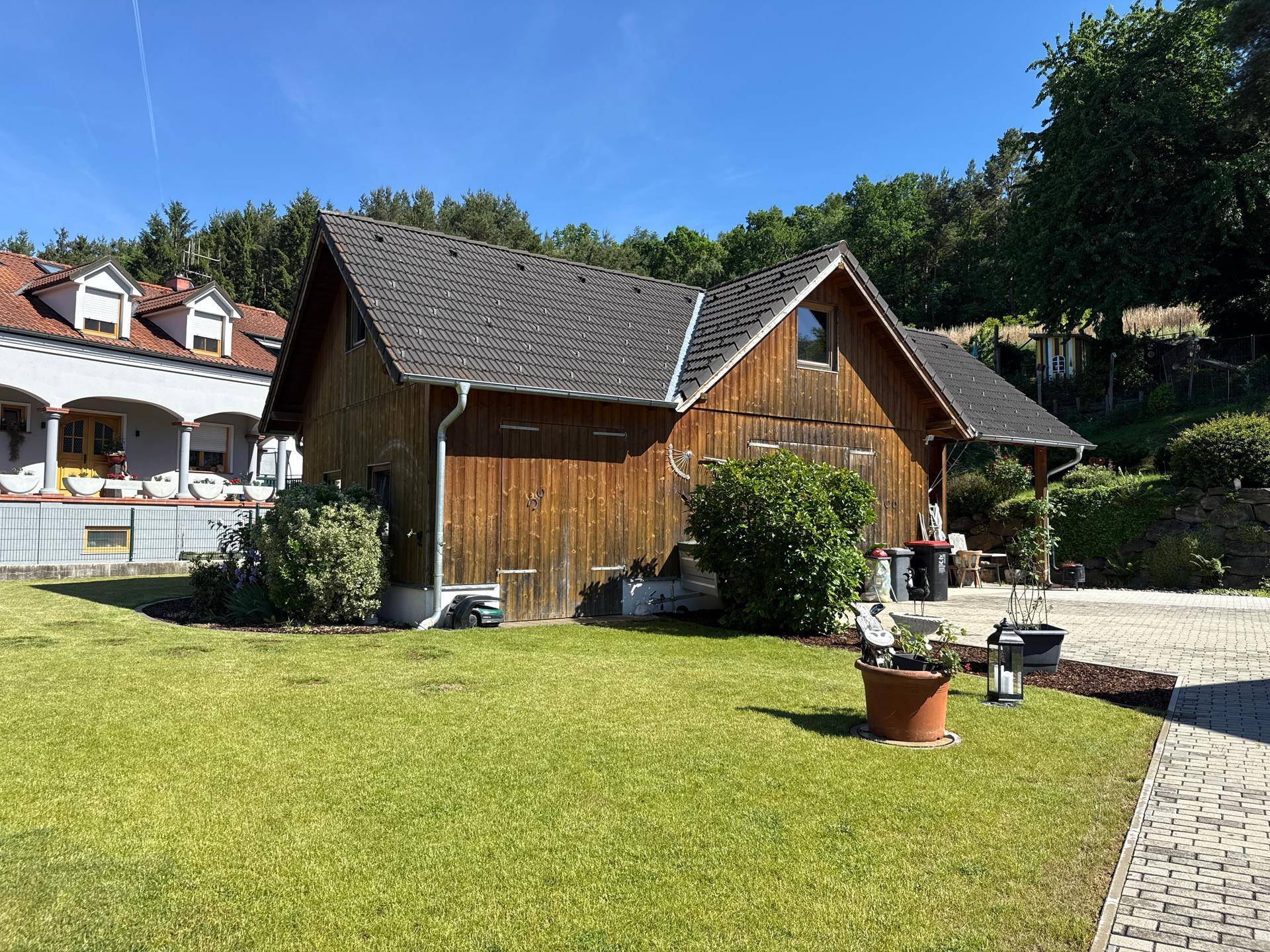 Rustikales Holzgebäude im Garten mit Rasenfläche und dekorativen Pflanzen in Töpfen.