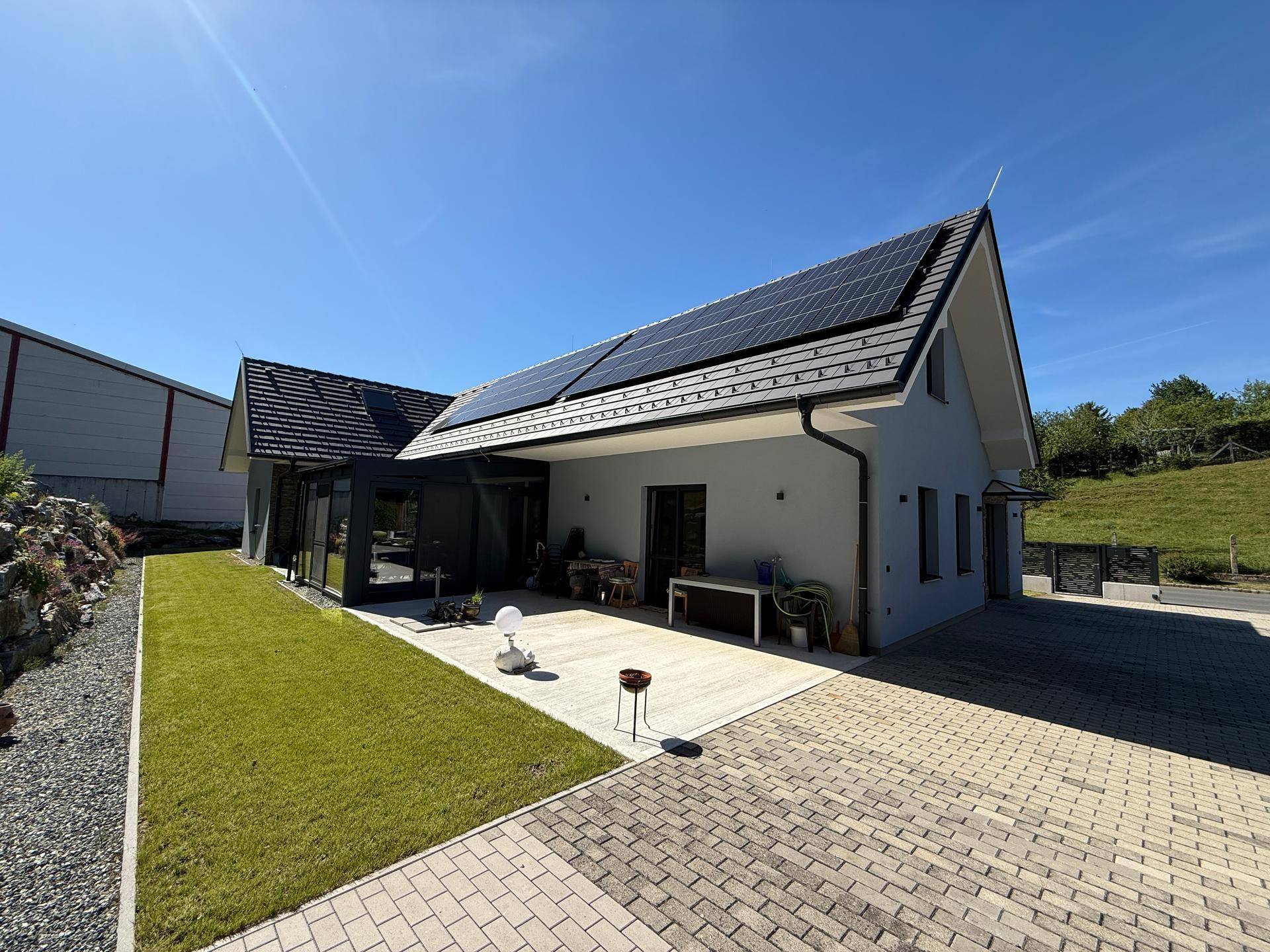 Modernes Haus mit Solaranlage, gepflasterter Terrasse, Rasen und dekorativer Felswand.